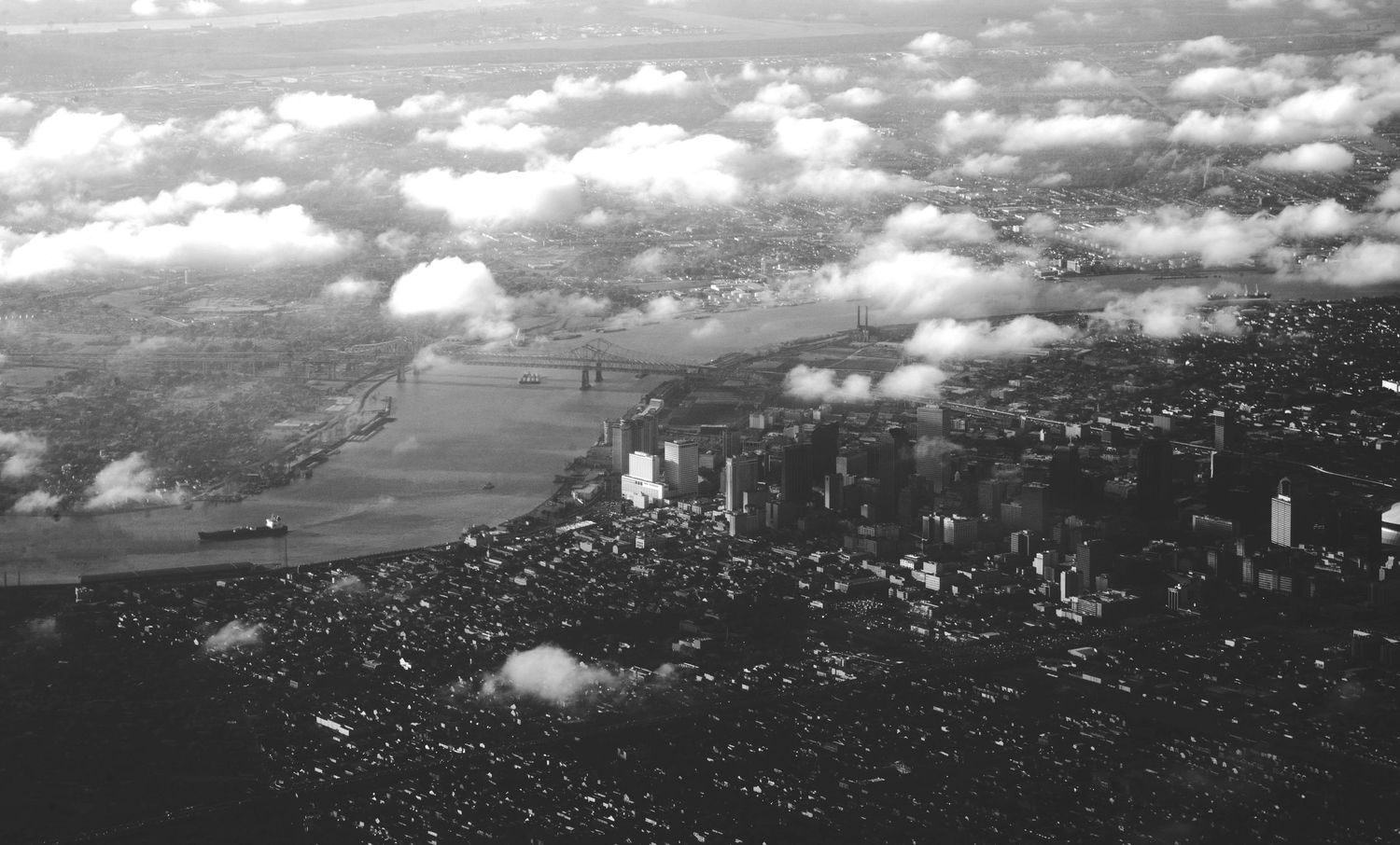 Black and white aerial view of a city skyline surrounded by clouds and a river.