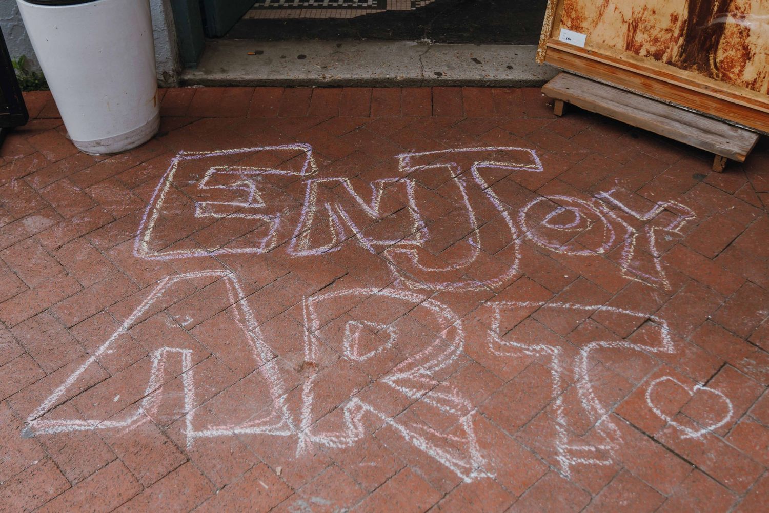 Chalk art on brick pavement reading Enjoy Art with a heart, outside an art studio entrance.