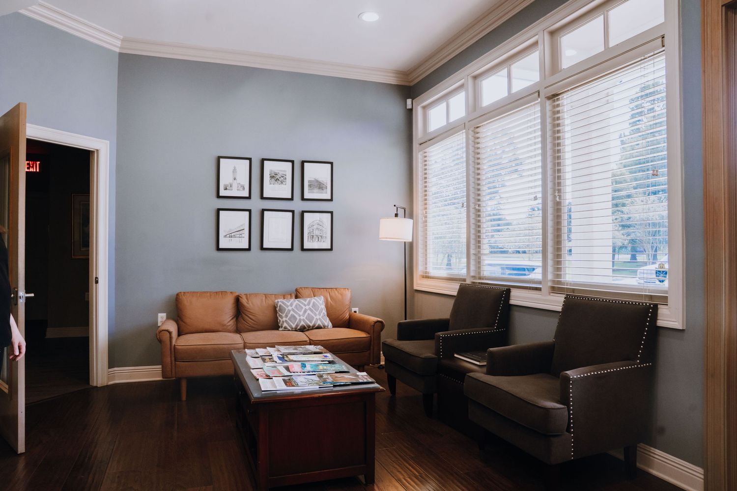 A cozy dental office waiting room with blue walls, a leather sofa, and large windows.