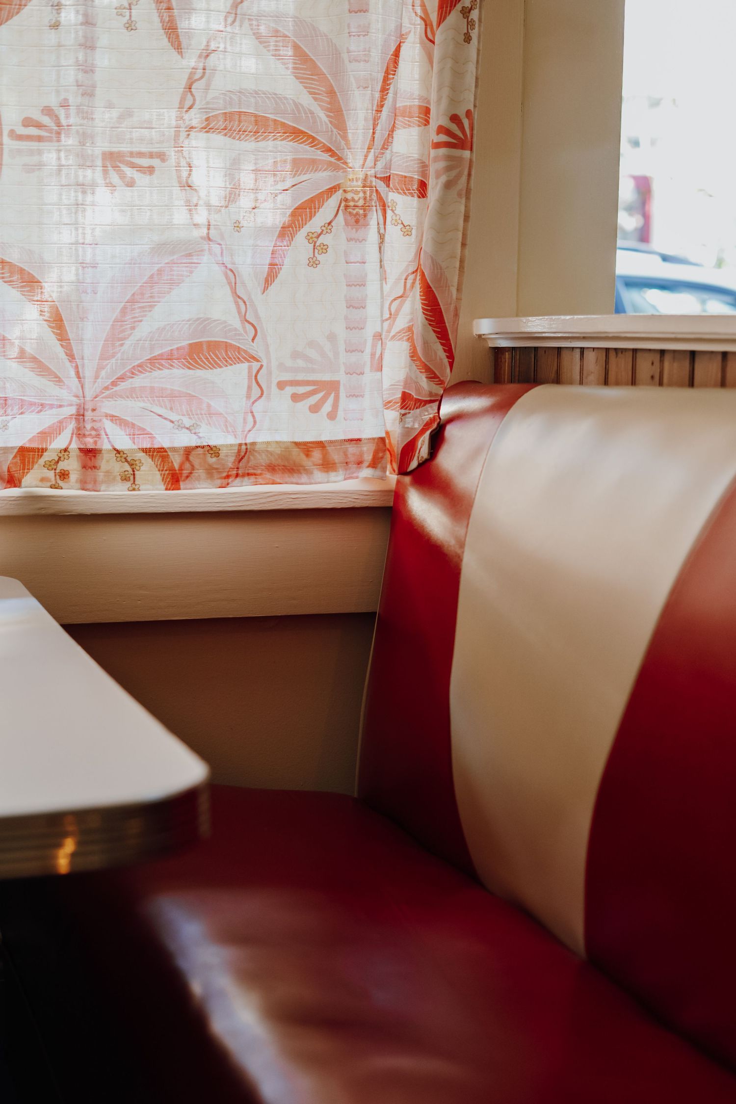 Vintage red and white leather diner booth seat beside window with tropical floral curtains.