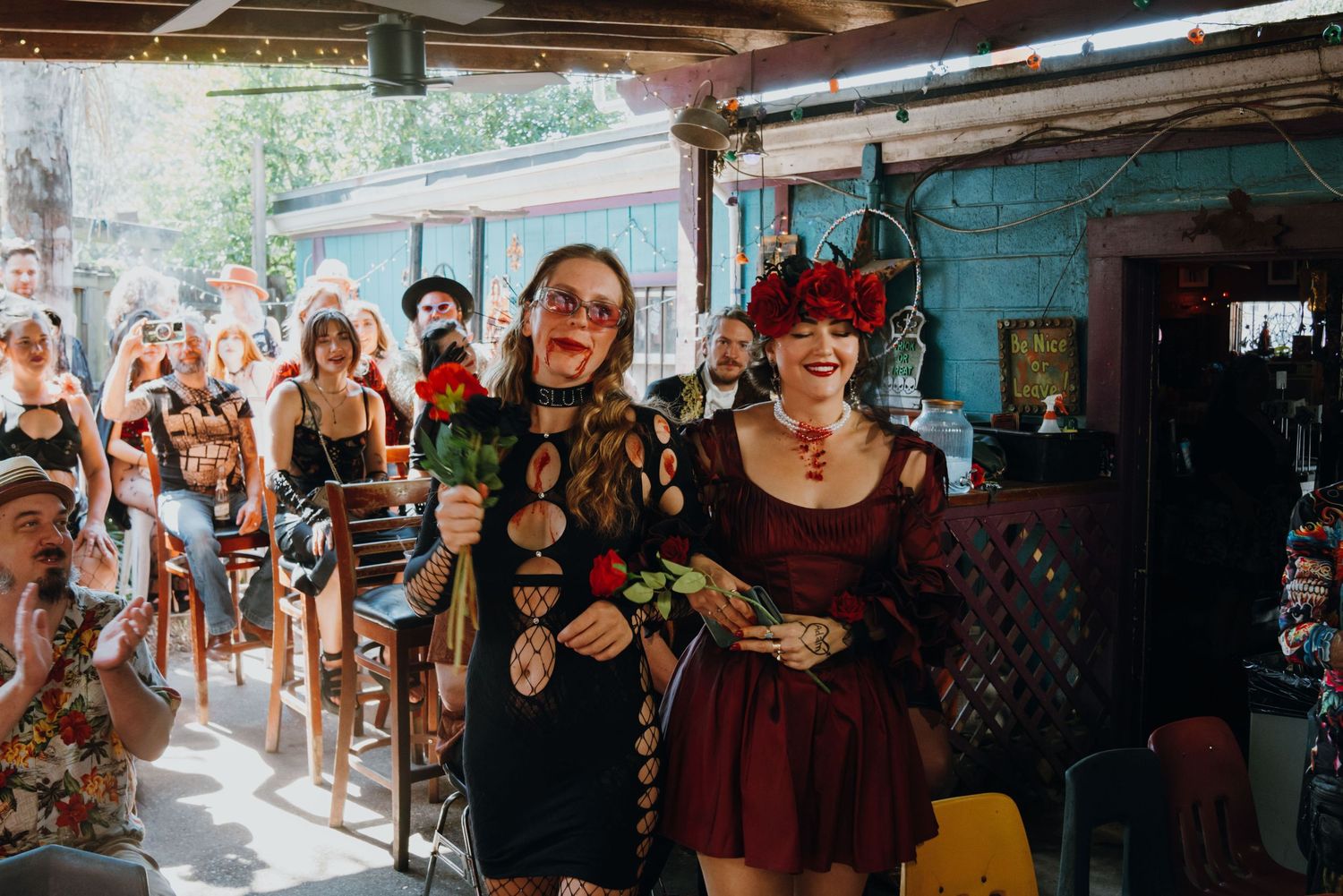 Two women in elaborate gothic costumes walk down the aisle at a colorful themed wedding ceremony.