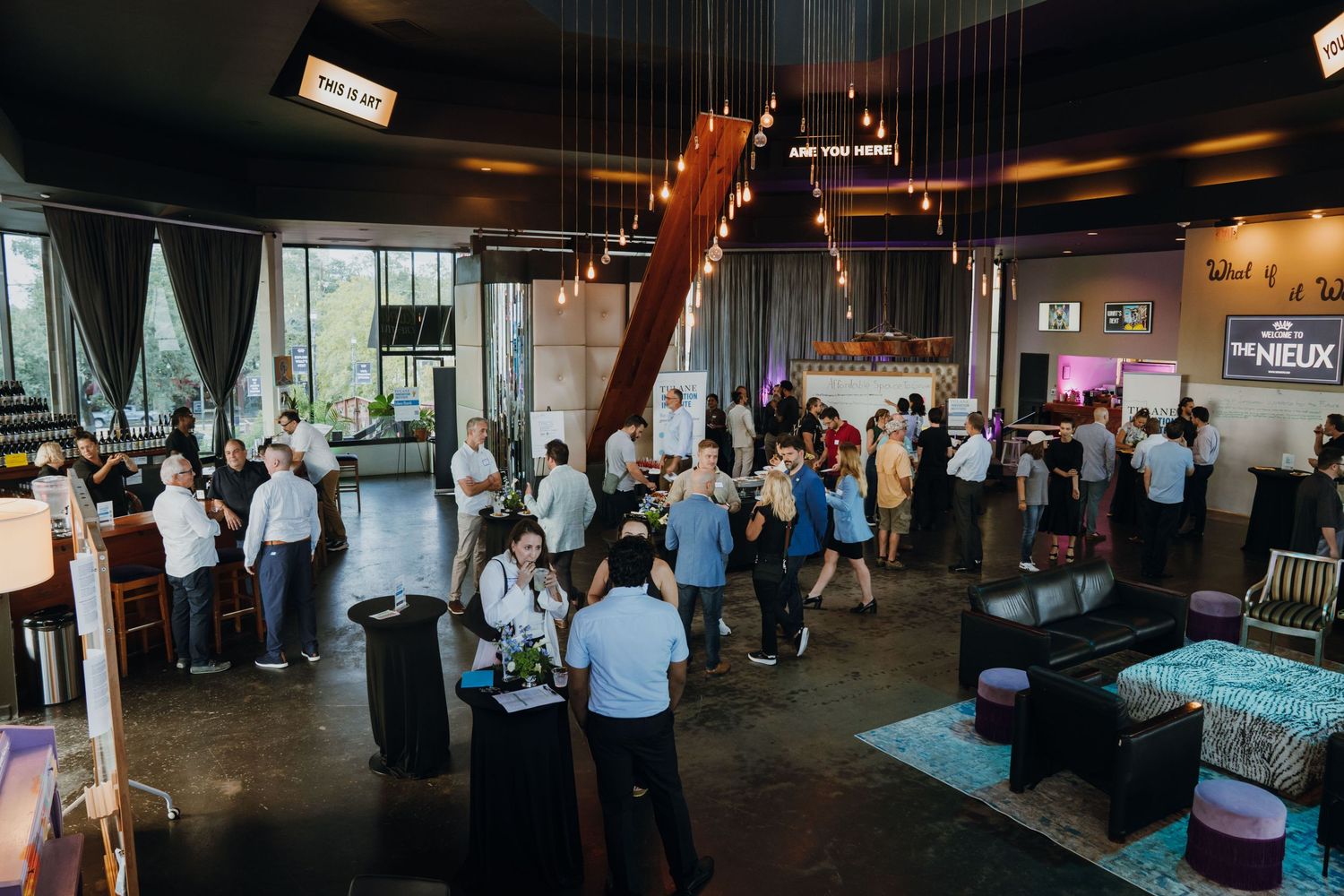 Guests mingle at an upscale indoor event venue with modern decor, pendant lights, and a lively social atmosphere.