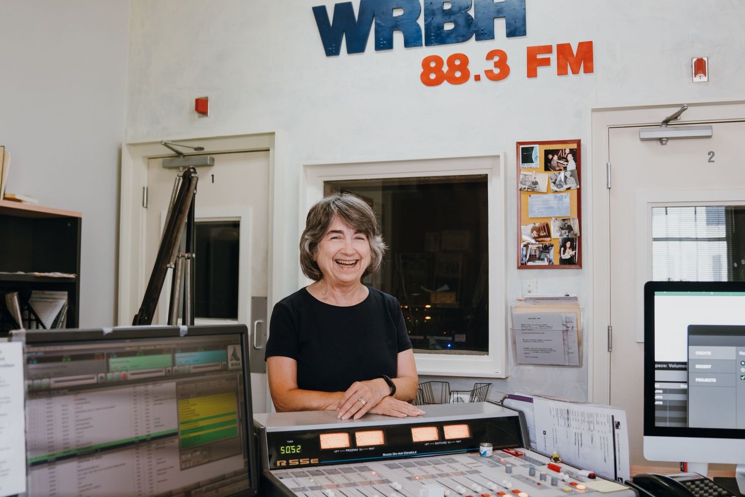 Smiling woman standing at the broadcast console inside WRBH 88.3 FM radio station studio.