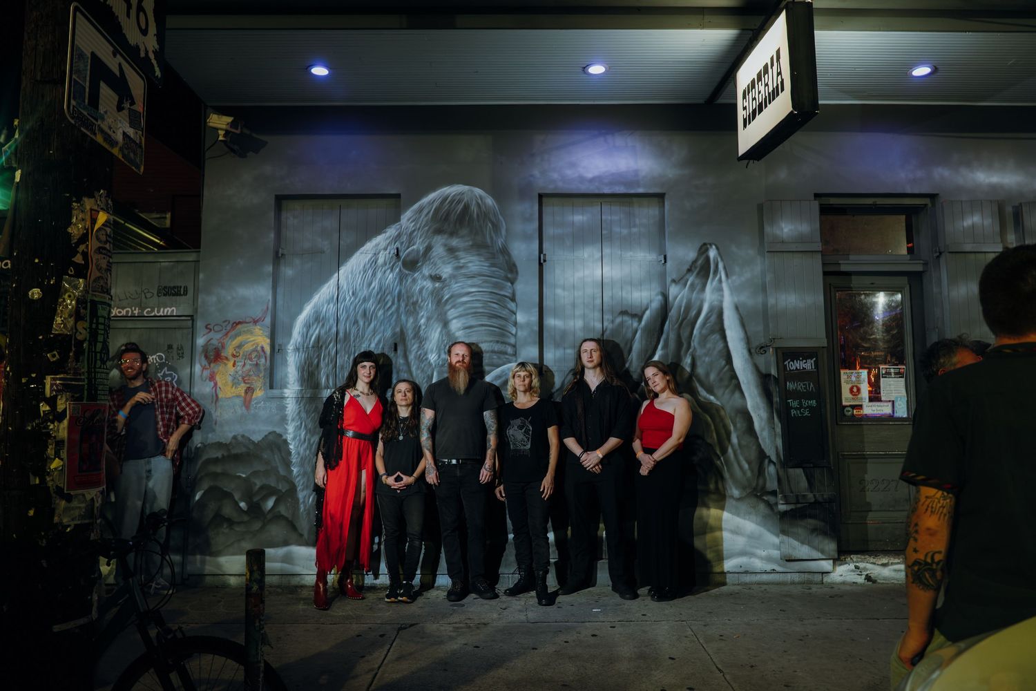Theater ensemble group photo at night in front of building with large elephant mural.