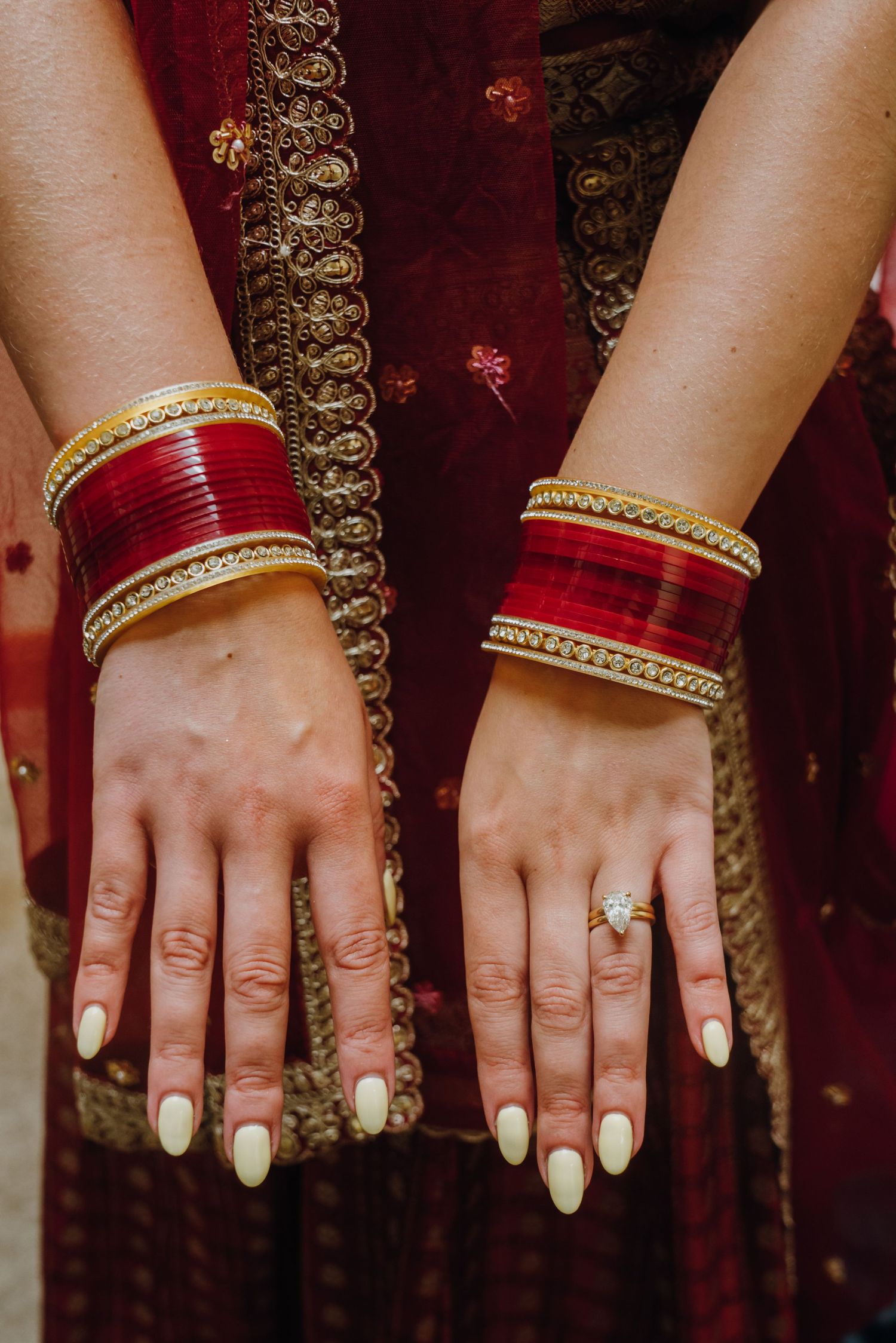 South Asian bride displays red and gold bangles with diamond engagement ring on both wrists.