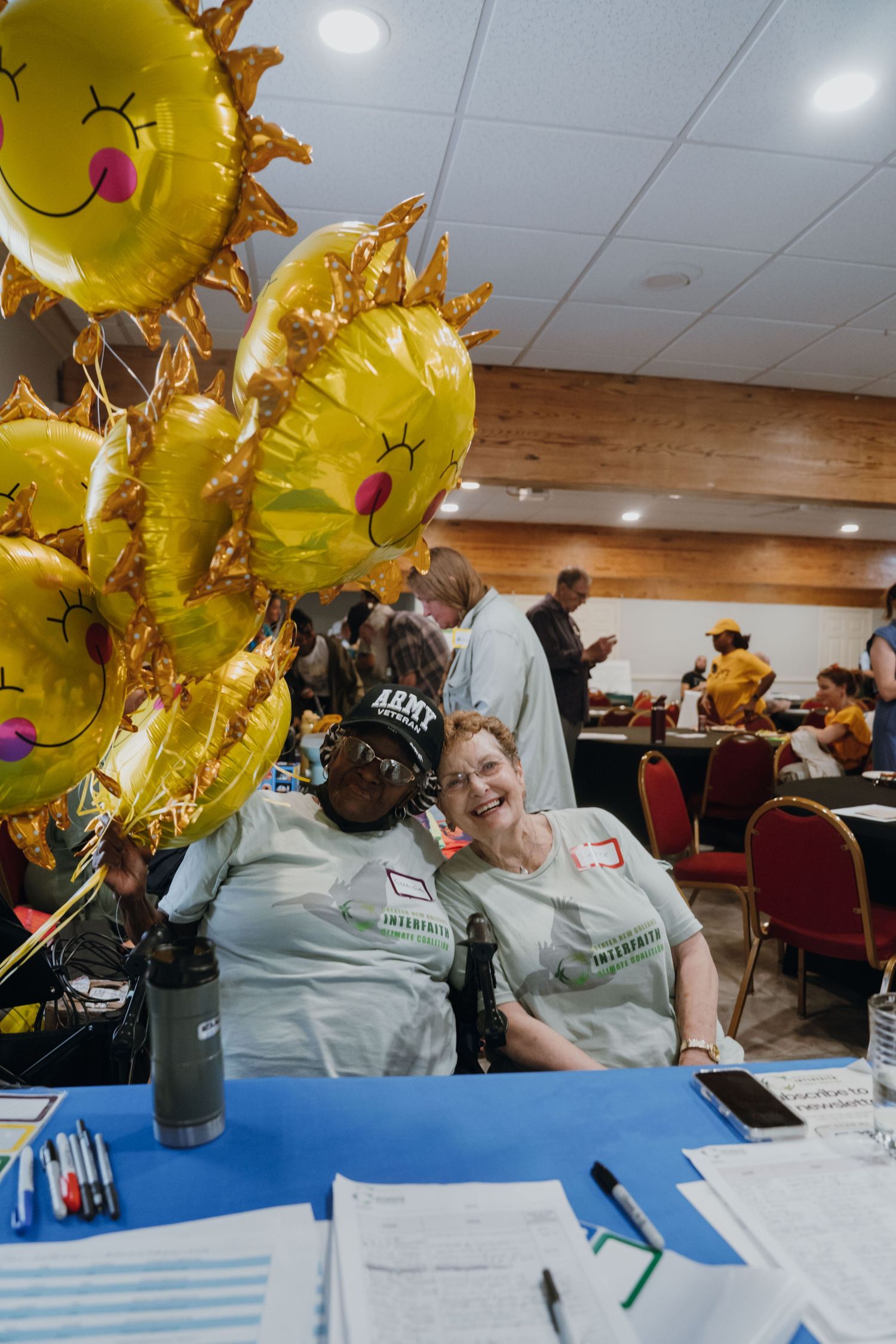 Two smiling volunteers in matching shirts pose beside golden sun-shaped balloons at an event.