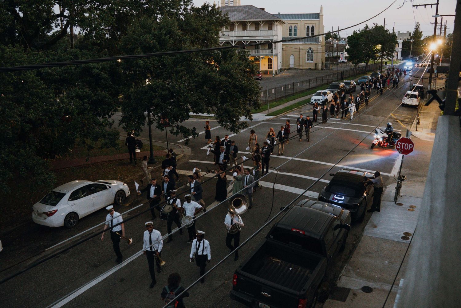 Aerial view of wedding guests participating in New Orleans second line parade at dusk.