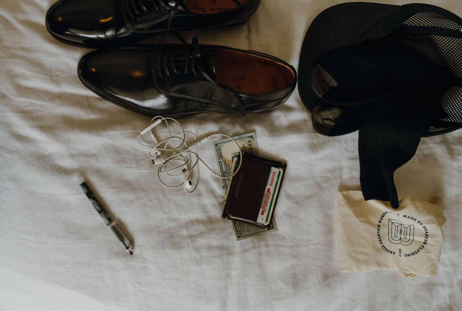 Groom wedding flat lay with black dress shoes, wallet, glasses, pen, and bow tie on white fabric. New Orleans, Louisiana, Mississippi
