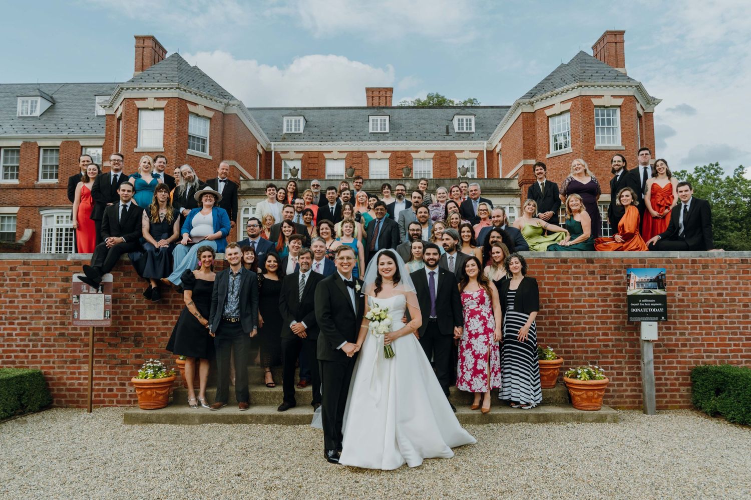 Full wedding party and guests pose in front of an elegant red brick estate on a cloudy day. New Orleans, Louisiana, Mississippi