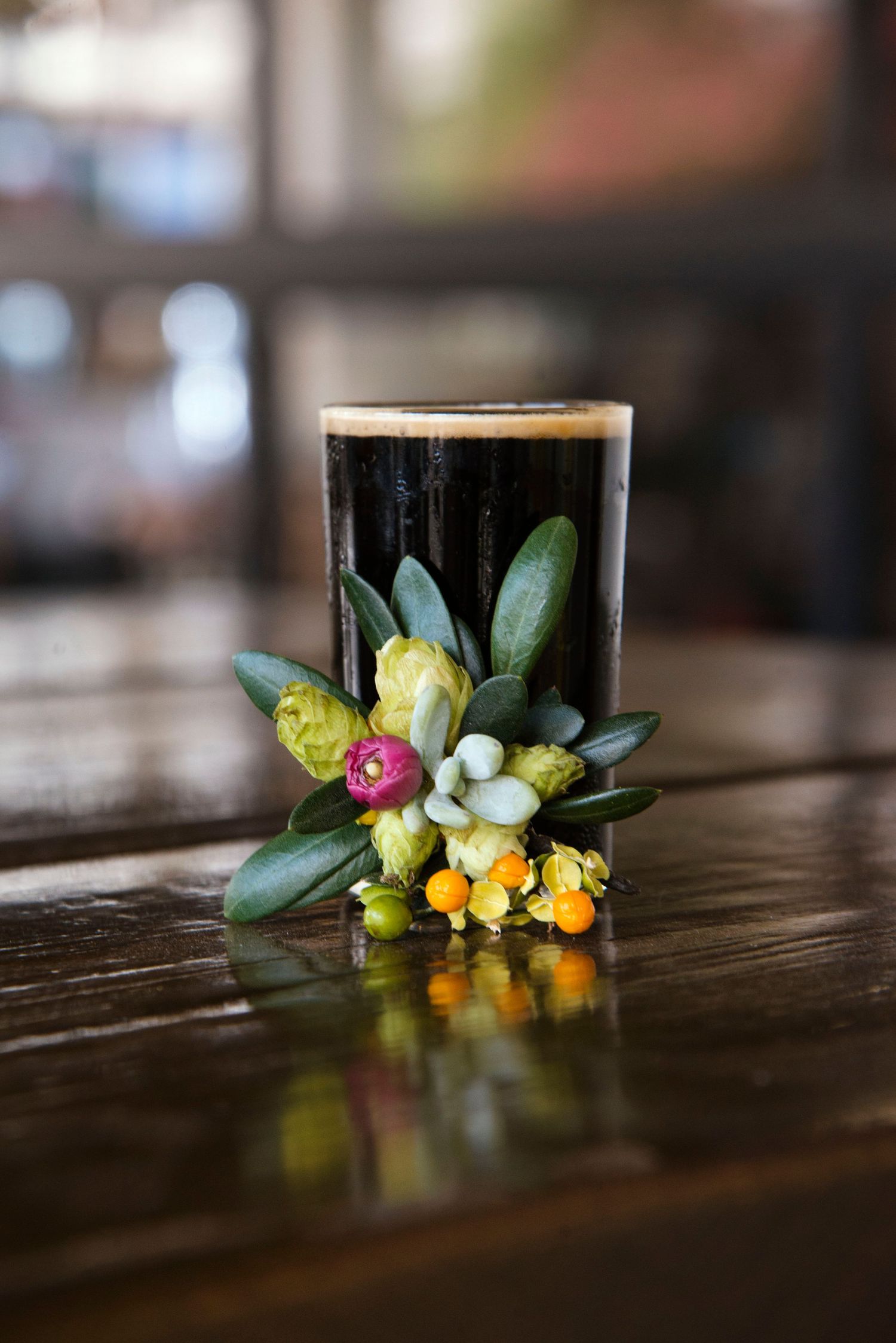 Dark stout beer glass decorated with colorful boutonniere flowers on wooden bar.