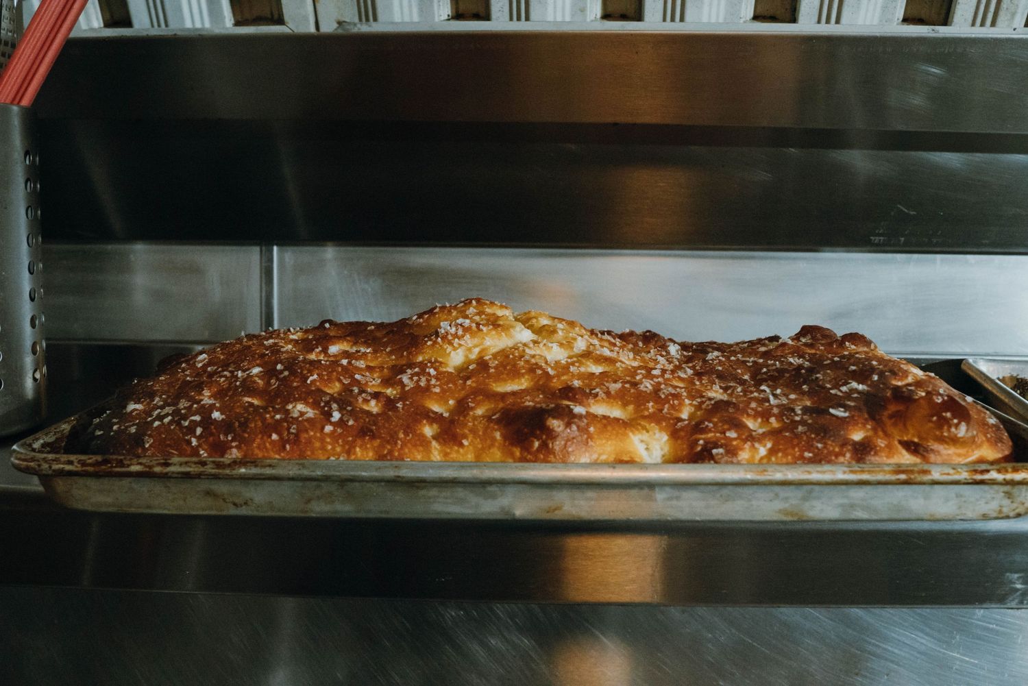Golden-brown freshly baked focaccia bread on a metal tray in a commercial oven.