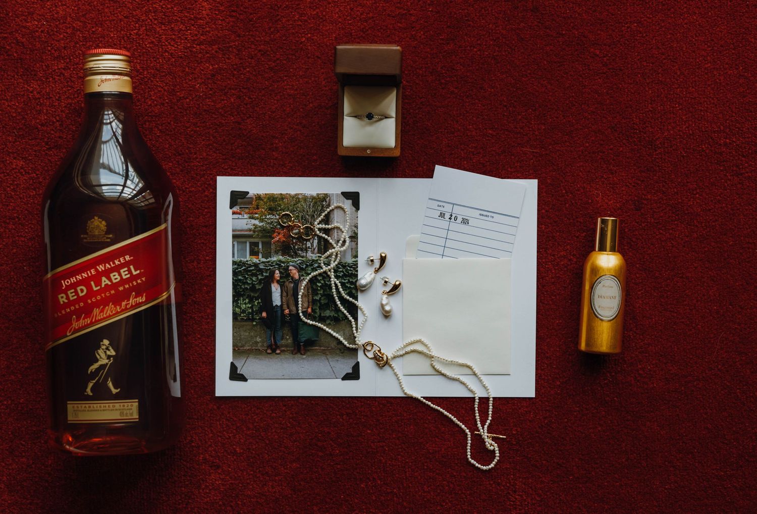 Johnnie Walker Red Label whisky bottle with wedding rings, photo, and gold perfume on red carpet. New Orleans, Louisiana, Mississippi