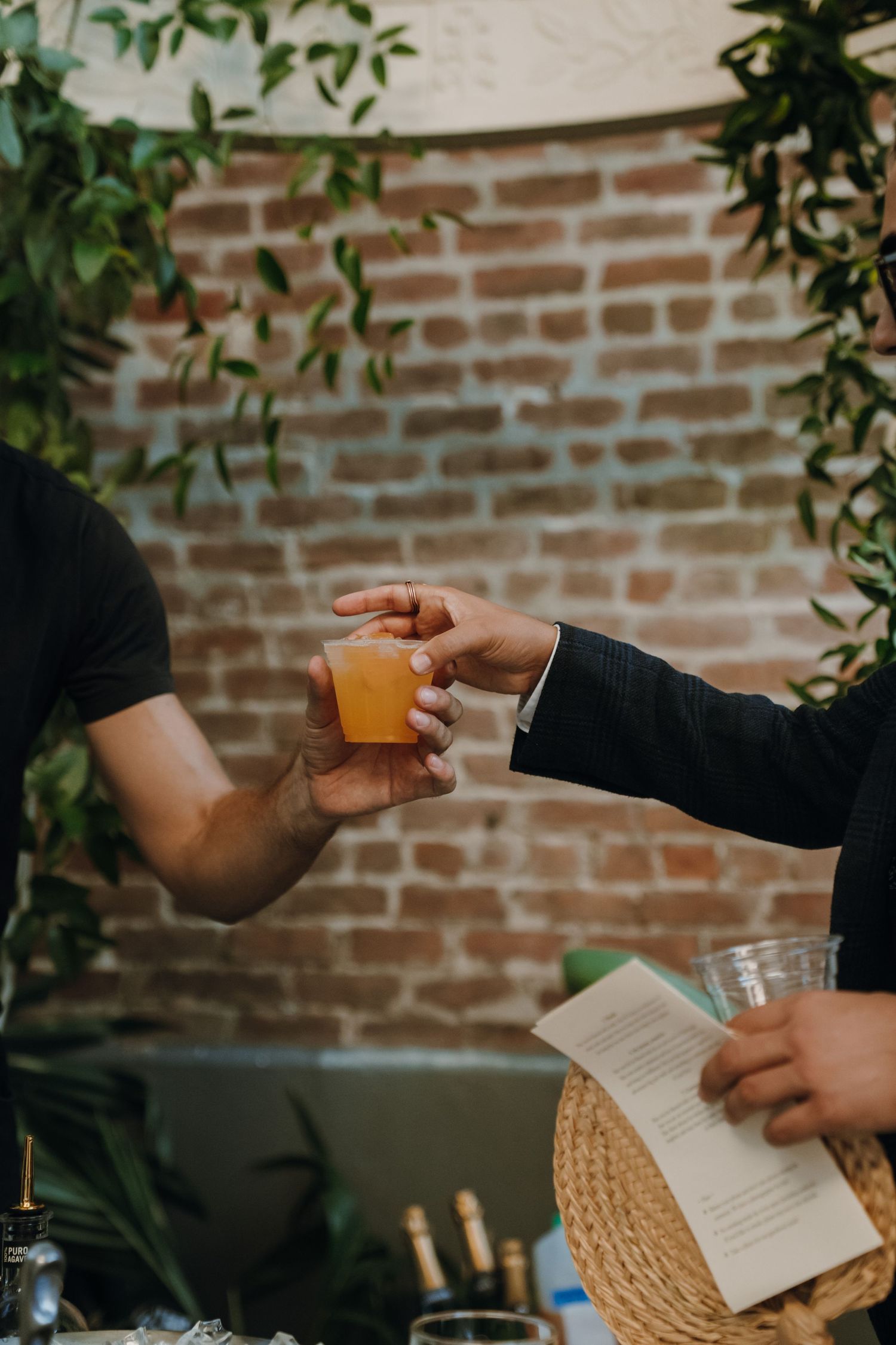 Bartender hands groom an orange cocktail drink at an outdoor wedding reception bar.