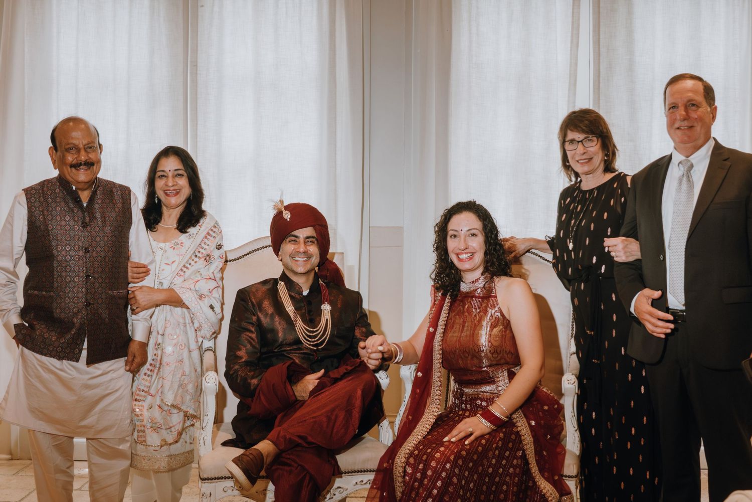Indian wedding family portrait with six guests in traditional and western attire smiling together.