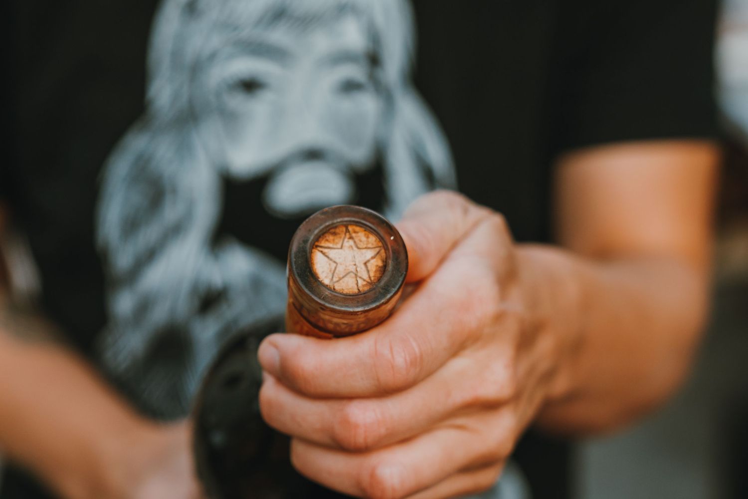 Close-up of a hand holding a wine bottle with a decorative wax seal stamp featuring a star emblem.
