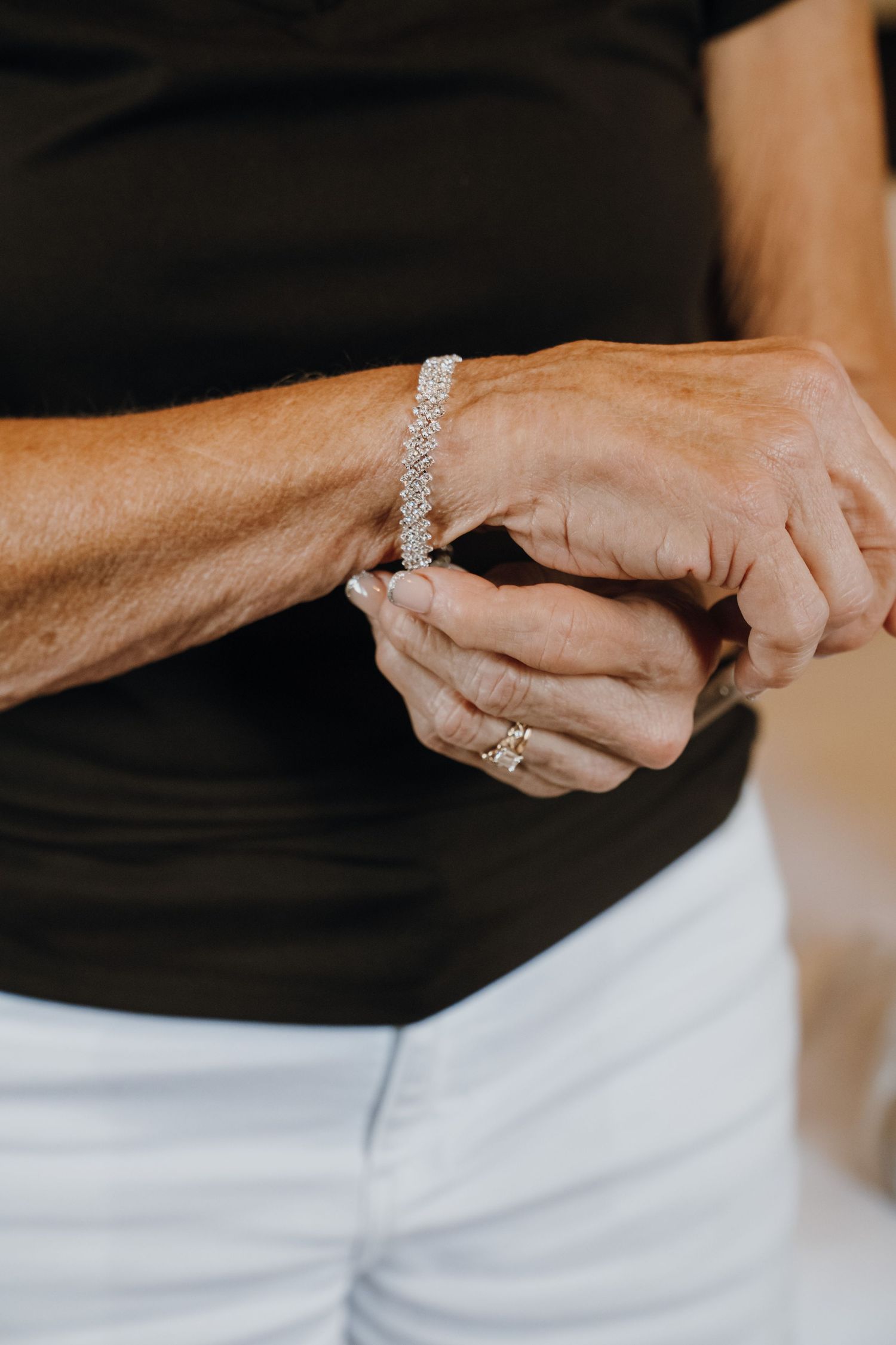 Close-up of woman fastening a sparkling diamond tennis bracelet on her wrist.