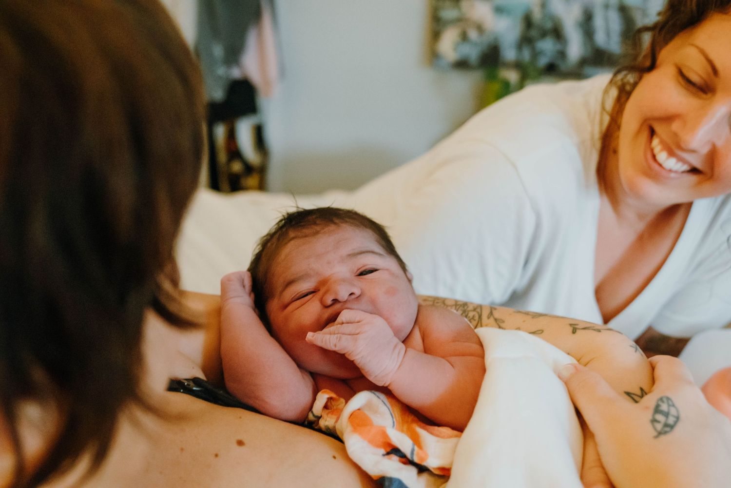 Newborn baby smiling while being held by mother after home birth with midwife smiling in background.