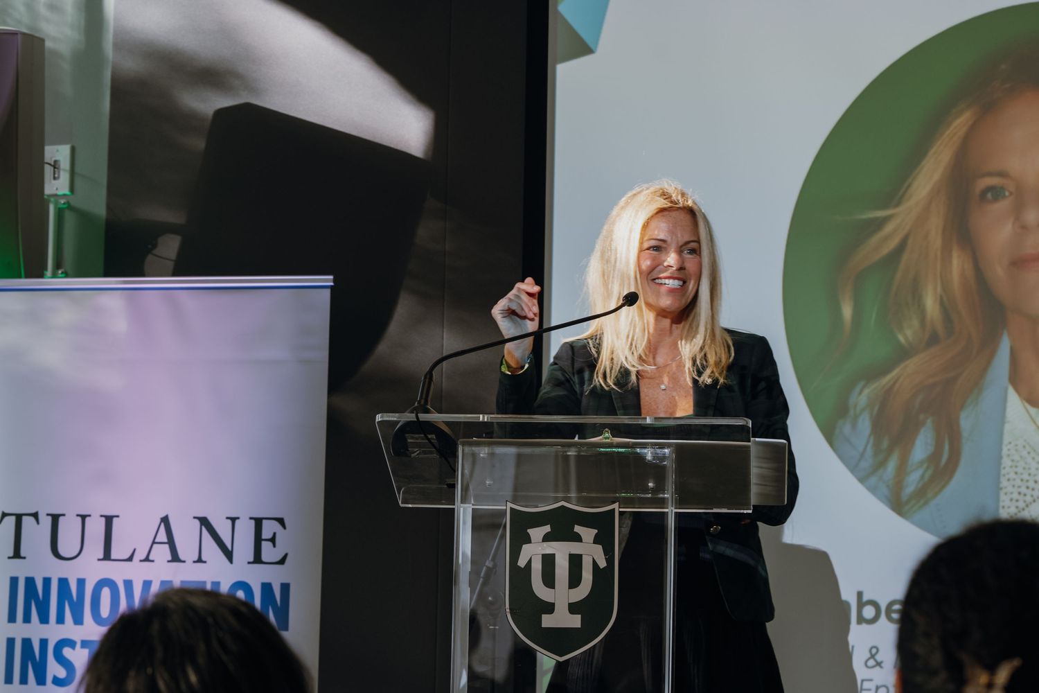 Blonde woman speaking at podium during Tulane Innovation Institute presentation event.