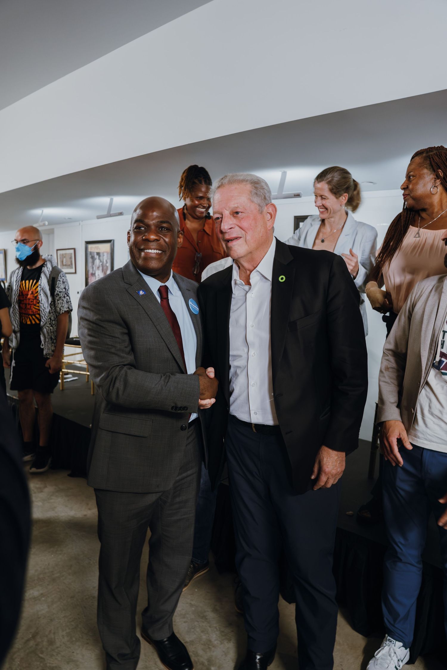 Two men shake hands and smile at an indoor networking event surrounded by a diverse crowd of attendees.