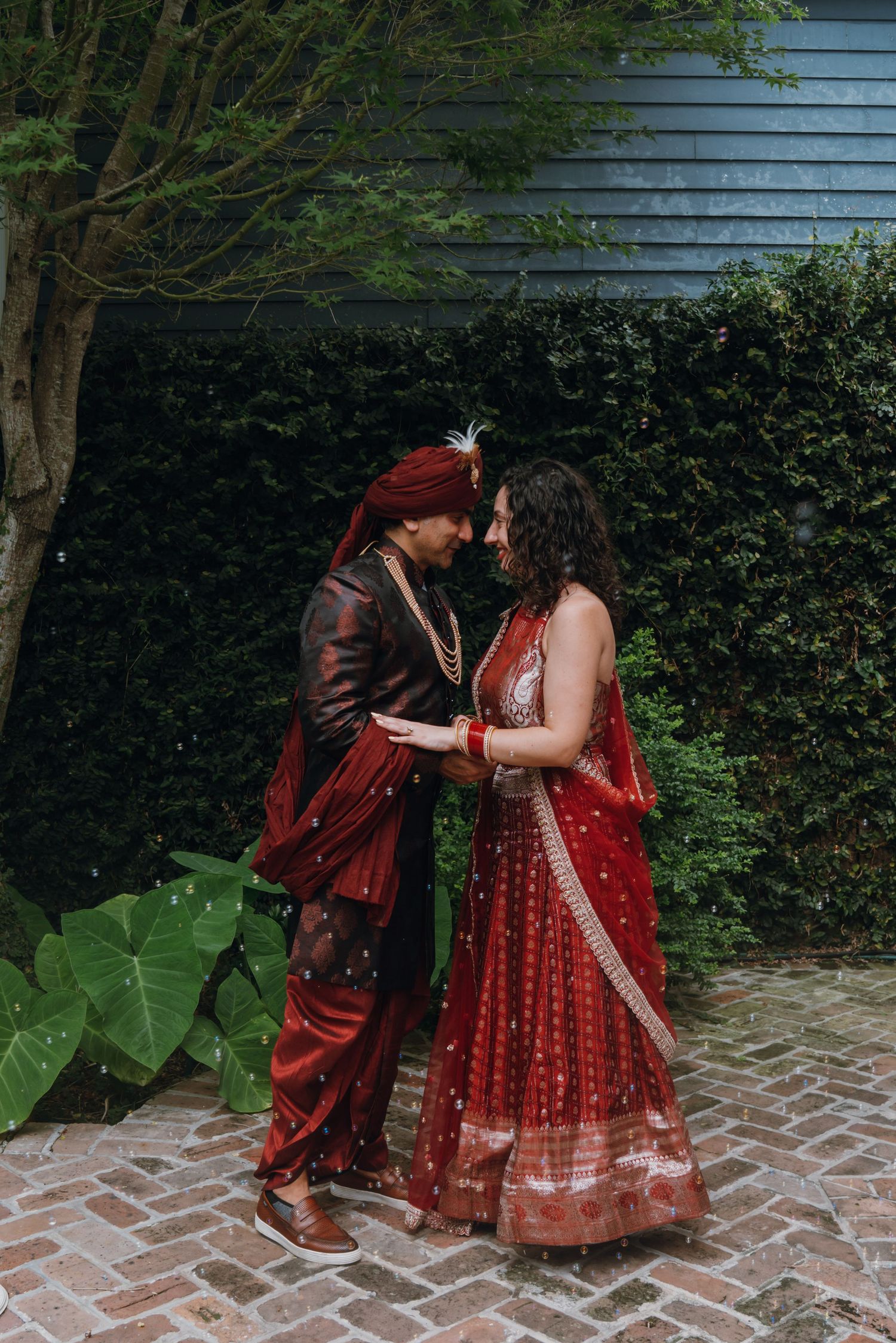 Indian bride and groom sharing an intimate forehead touch moment in traditional red attire.