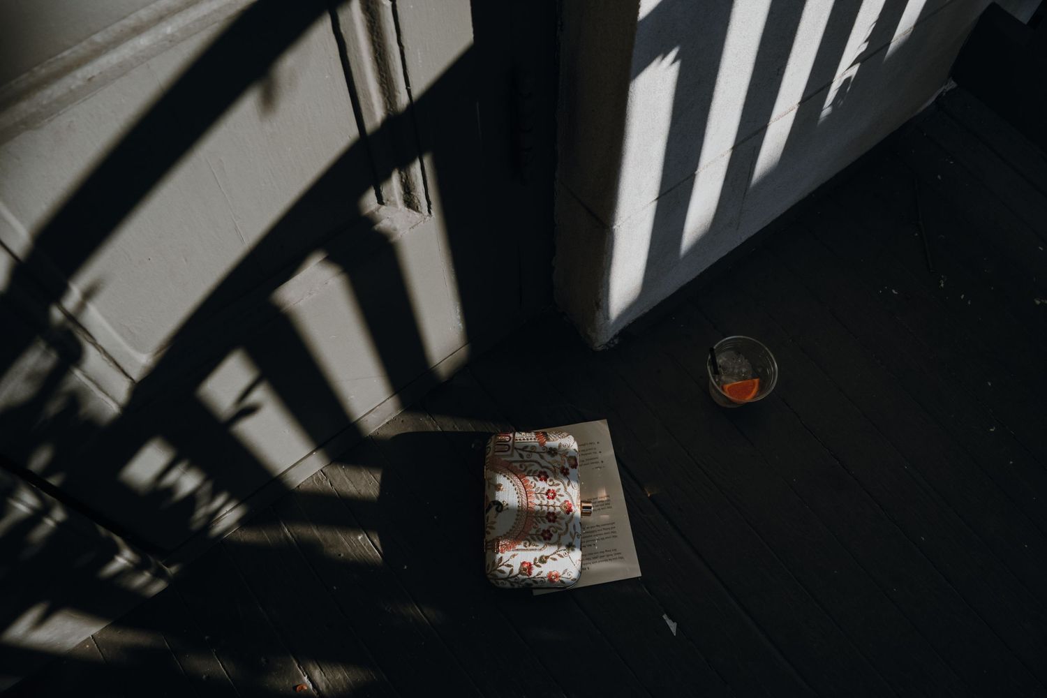 Rolled wedding scrolls and amber drink rest on dark floor with dramatic palm leaf shadows.