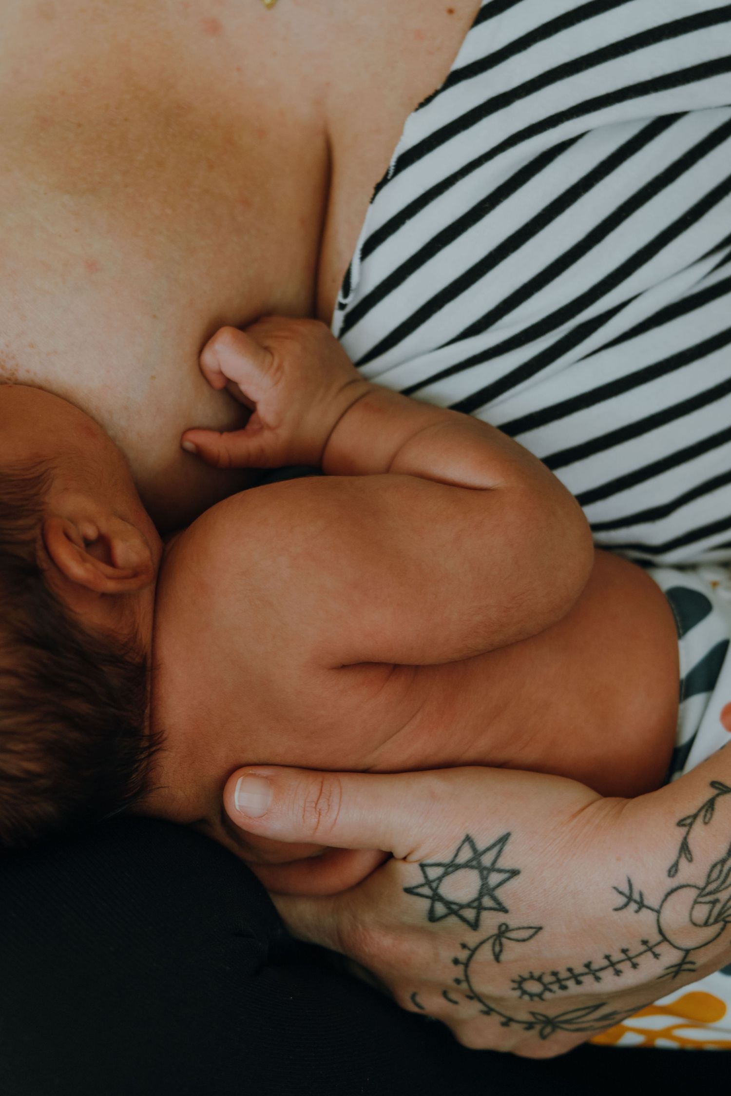 Close-up of tattooed mother breastfeeding newborn baby with star tattoo visible on hand. New Orleans, Louisiana, Mississippi