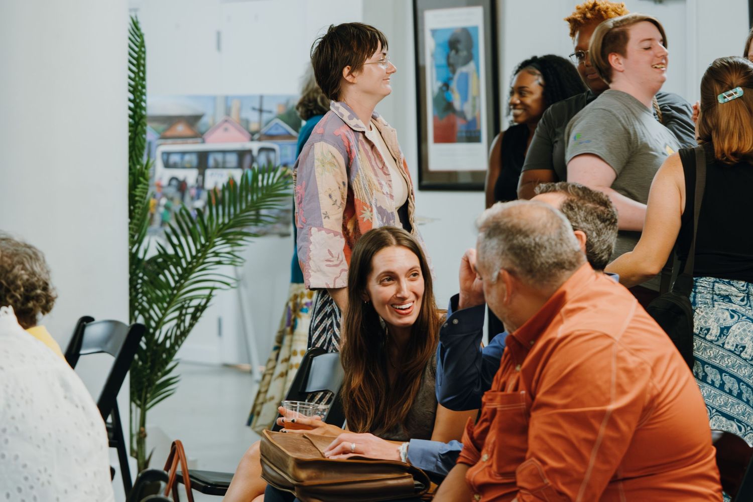 People socializing at an art gallery event, with a smiling woman engaged in conversation with a man in an orange shirt.