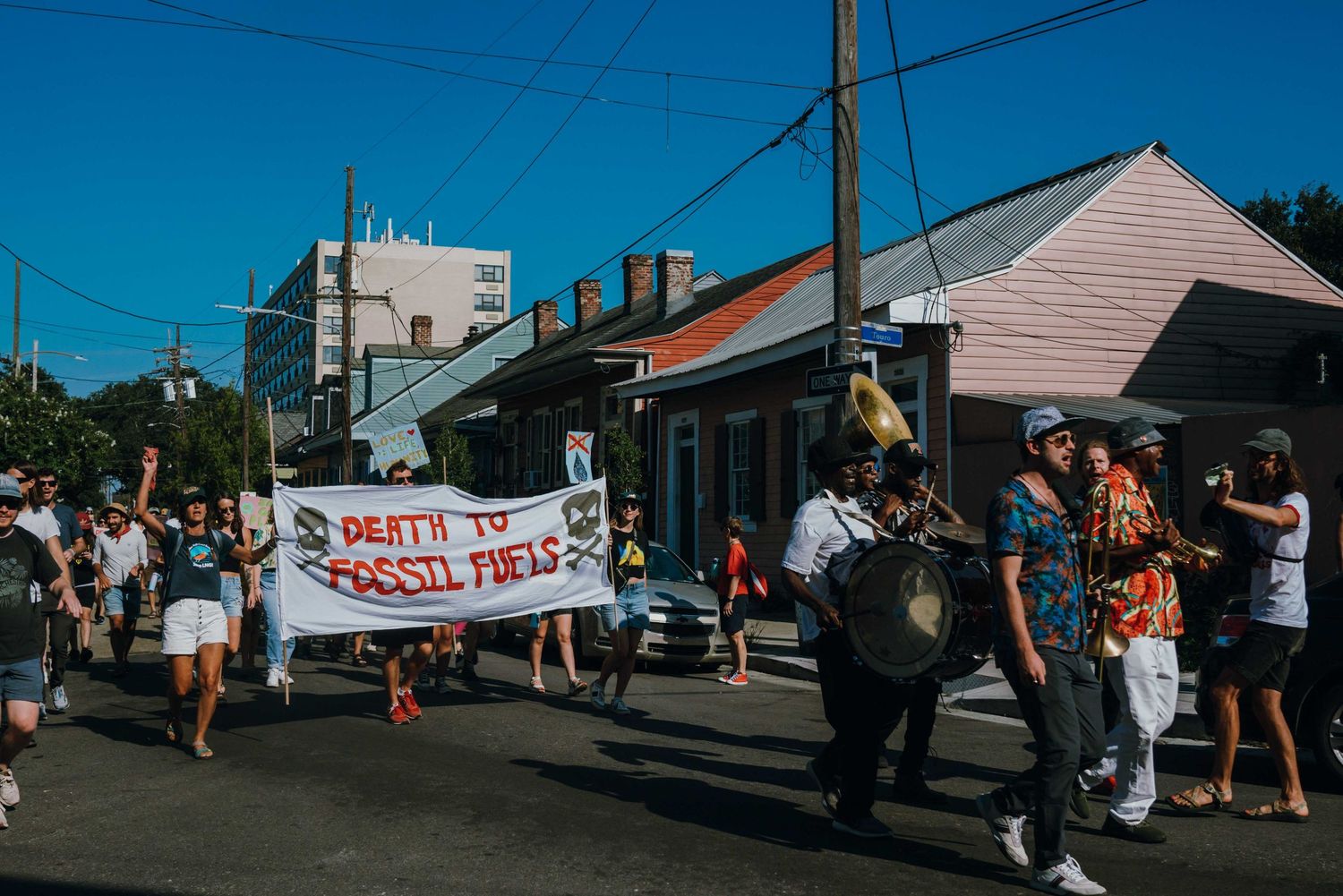 Protesters march down a street holding a Death to Fossil Fuels banner on a sunny day.