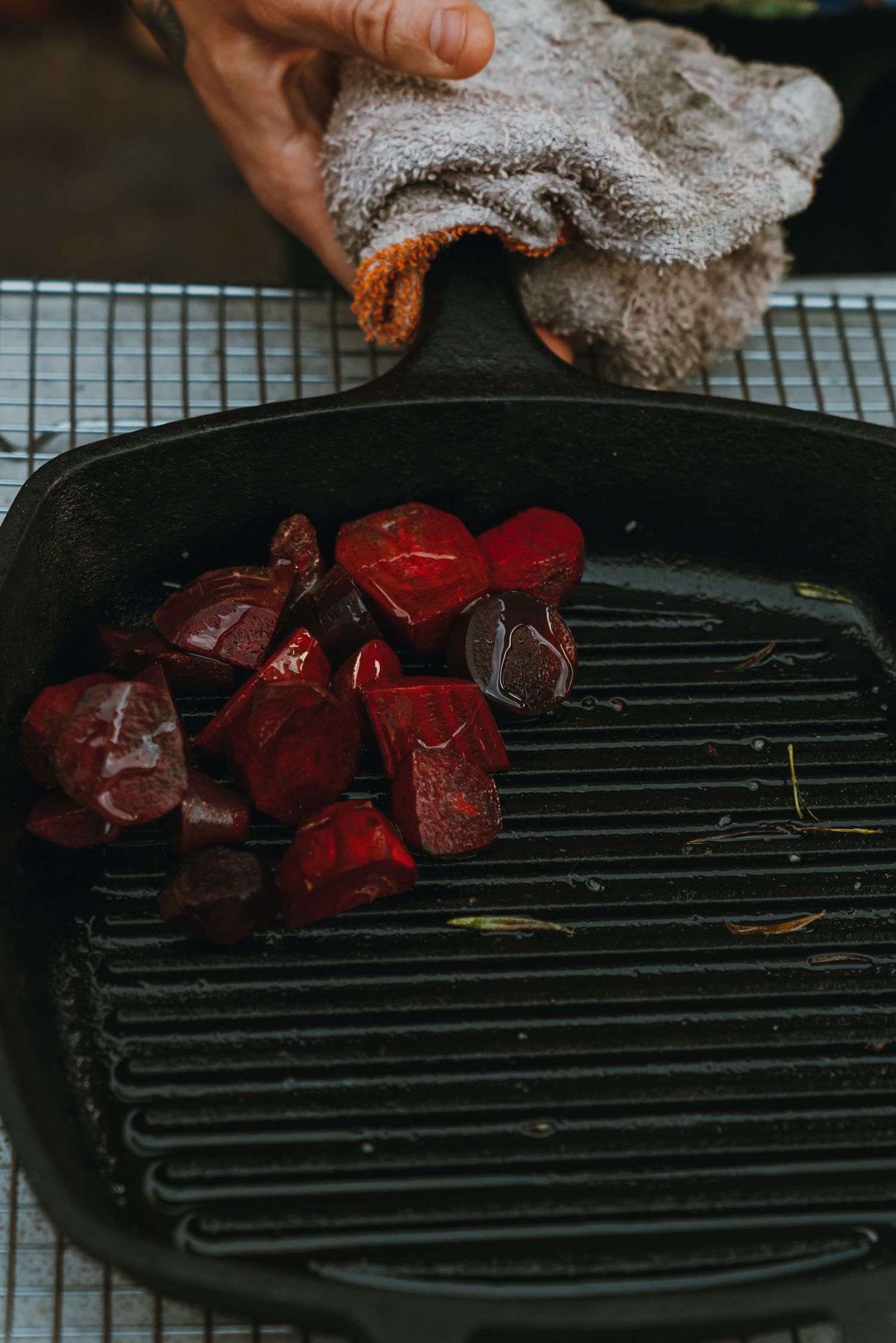 Roasted red beets in a cast iron grill pan being handled with a cloth towel.