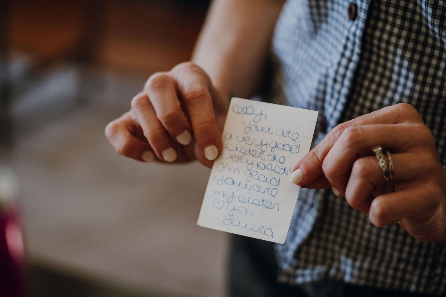 Close-up of hands holding a small handwritten note card with a gold wedding band visible.
