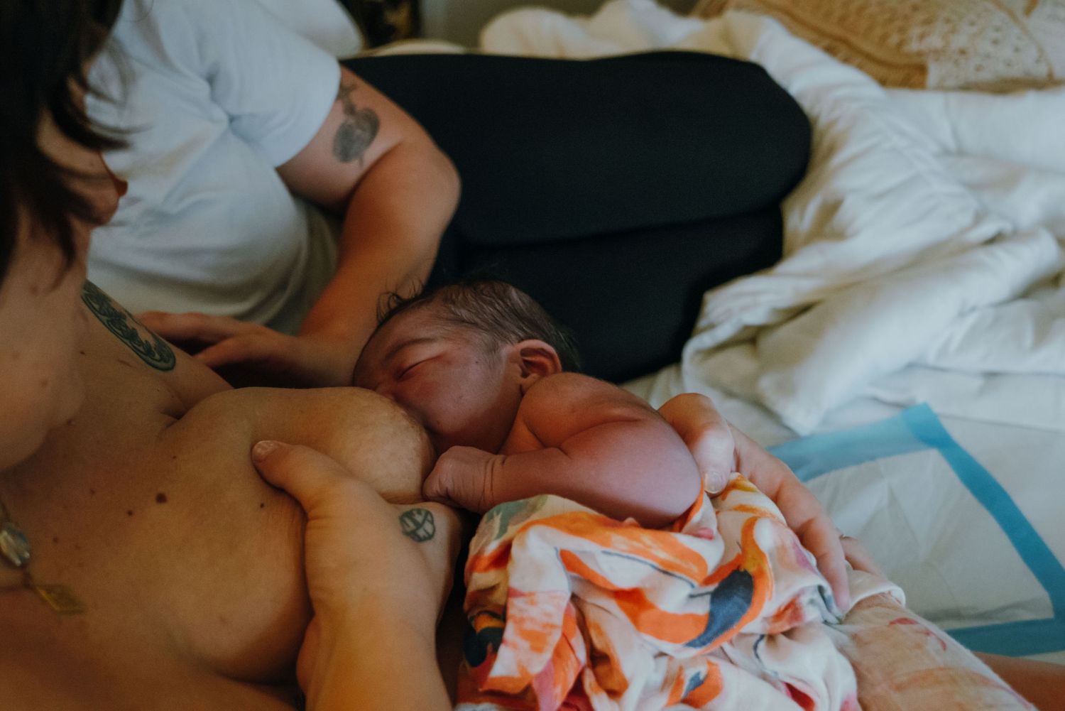 Mother breastfeeds newborn baby skin-to-skin on a bed after home birth.