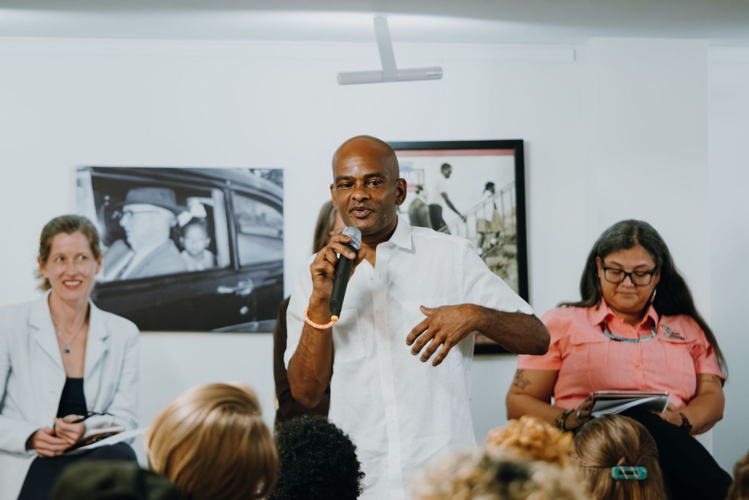 Man in white shirt speaking passionately to seated audience at community discussion panel.