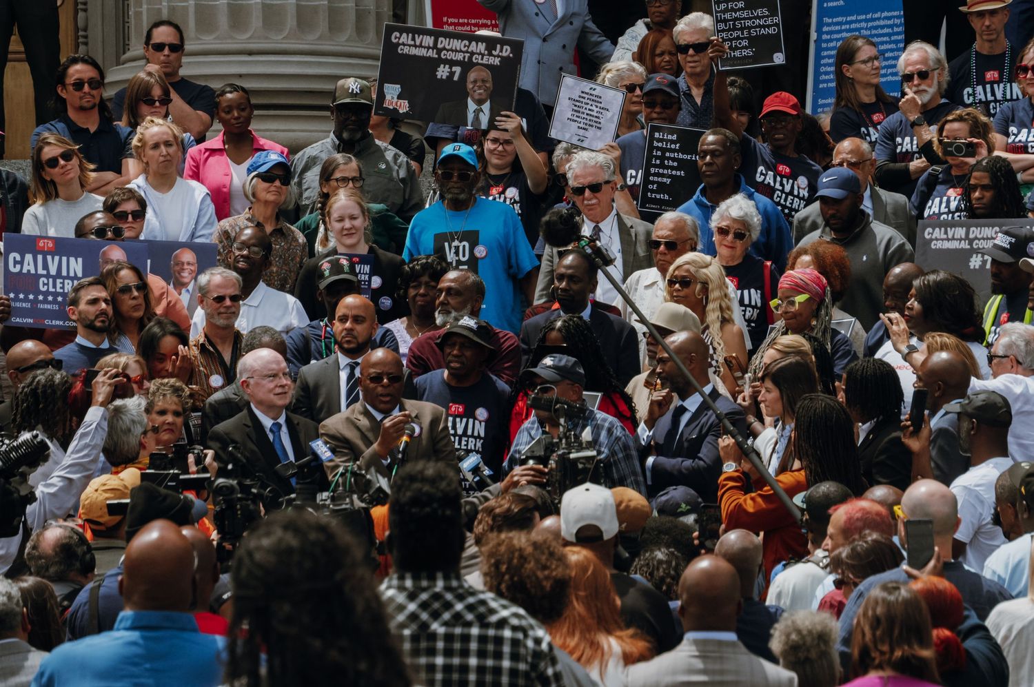 Large crowd gathered at a political rally holding campaign signs for candidate Calvin in an urban setting.