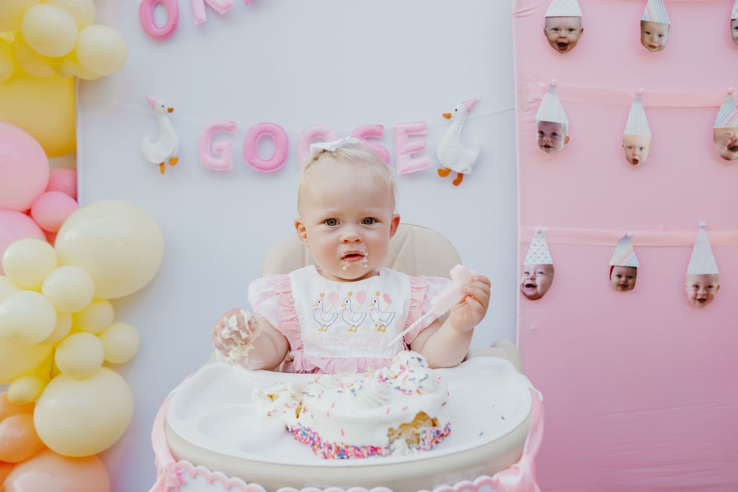 Baby girl in high chair enjoying her first birthday smash cake at a pink party.