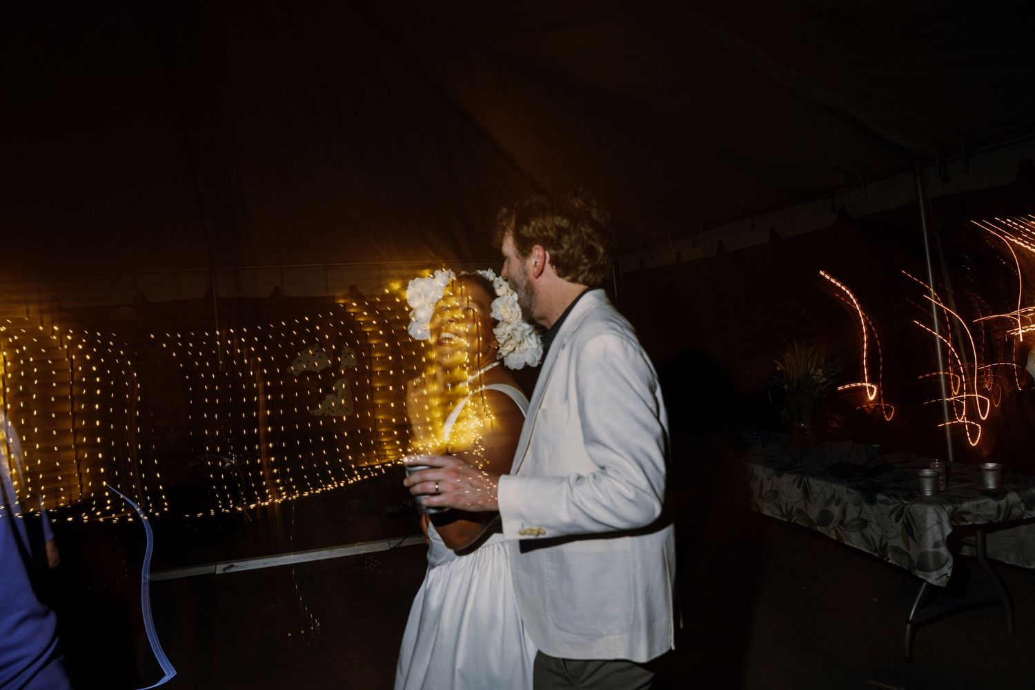 Couple shares a kiss on the dance floor under warm fairy lights at their wedding reception.