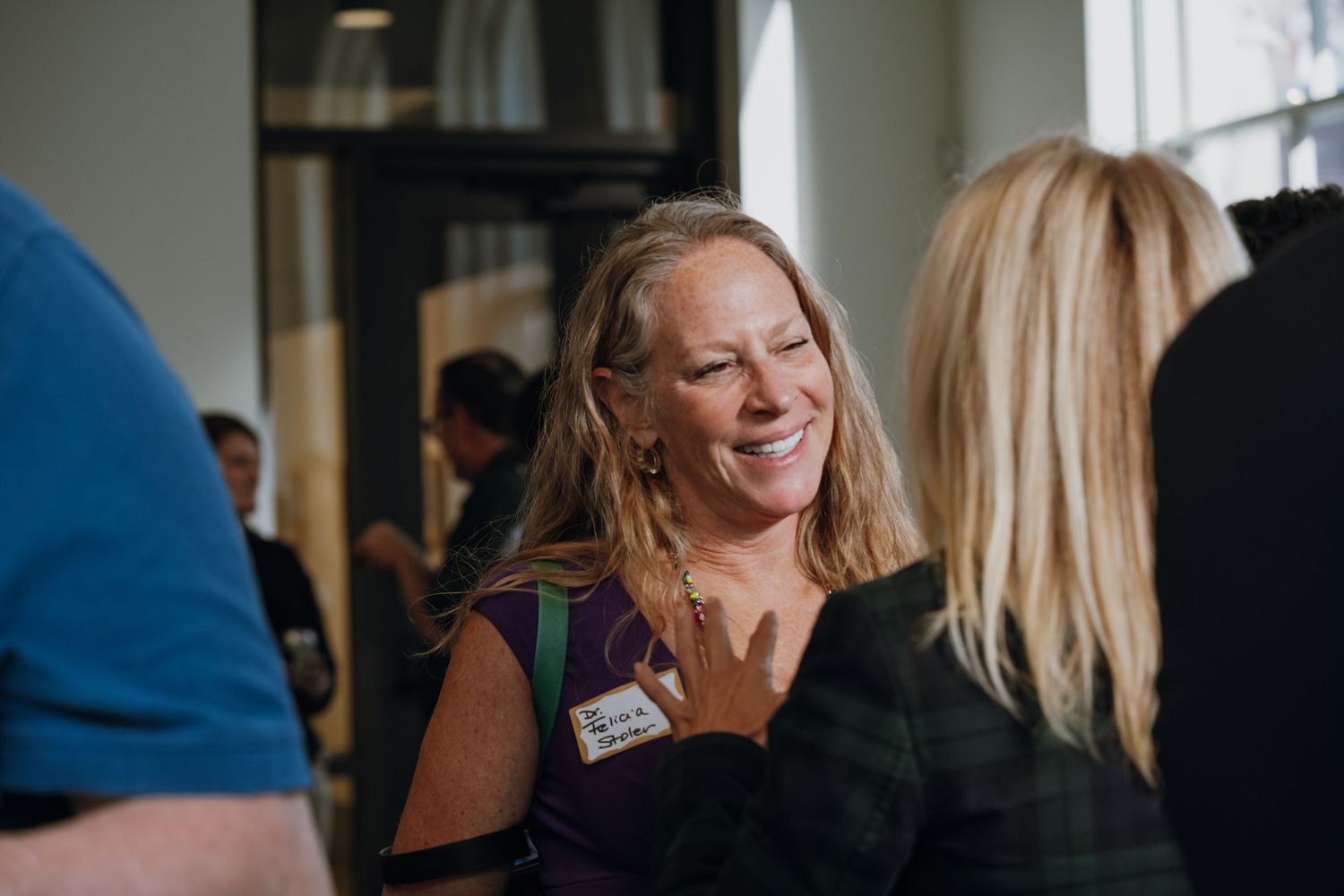Smiling woman with long blonde hair wearing a name tag at a professional networking event.