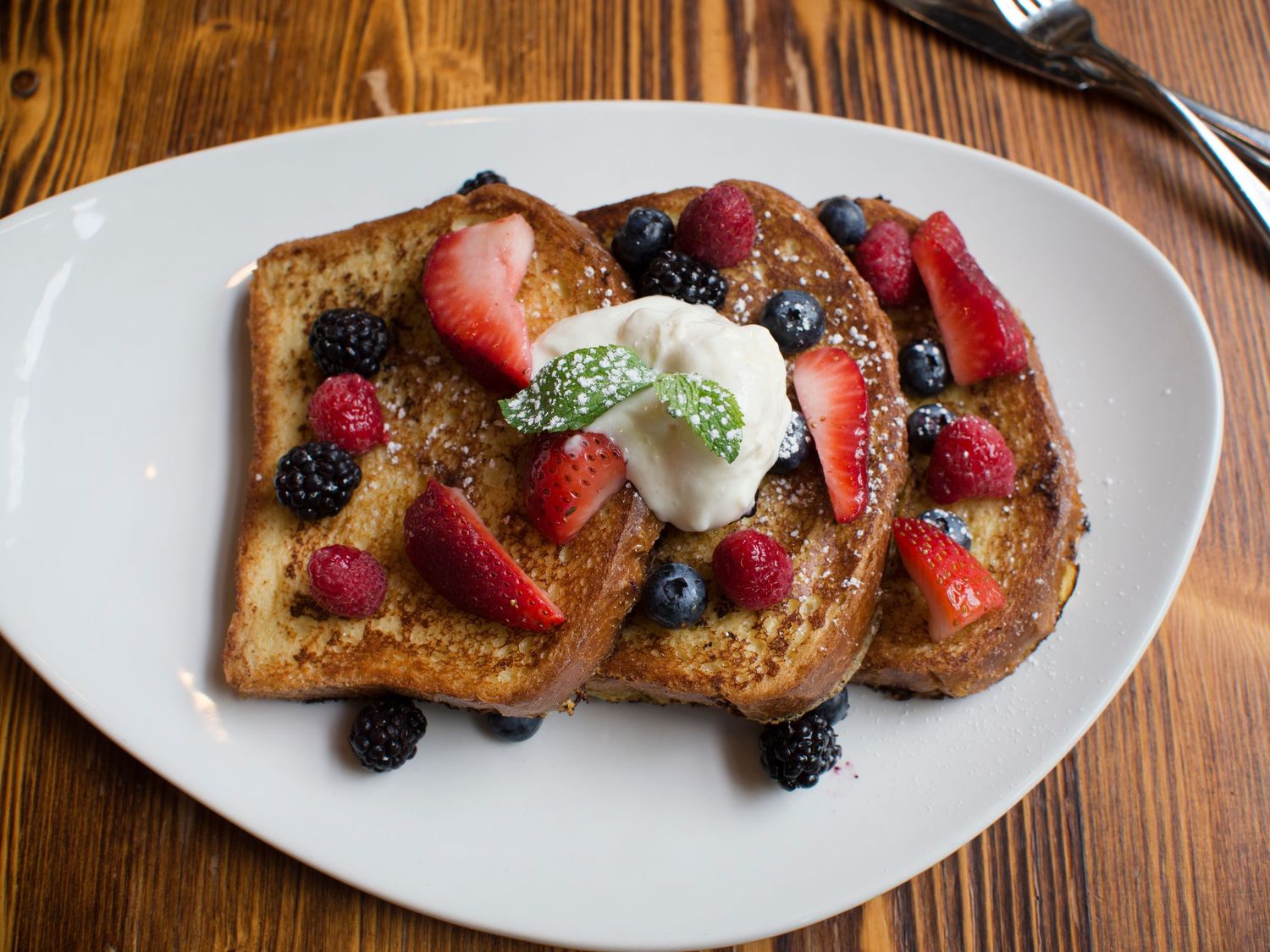 French toast topped with fresh strawberries, blueberries, blackberries, and whipped cream on a white plate.