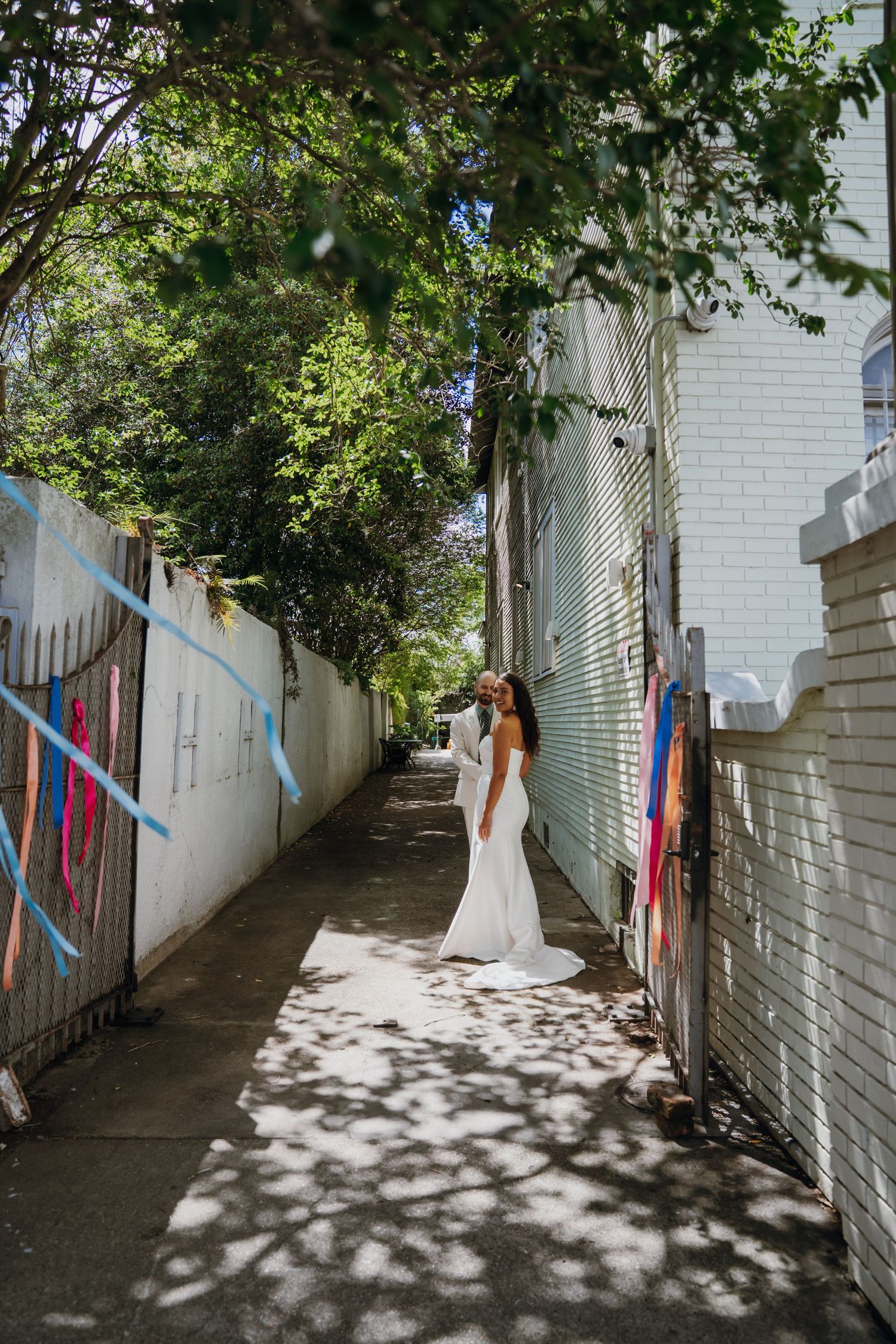 Bride in a white wedding gown standing in a sunlit alley with colorful graffiti walls.