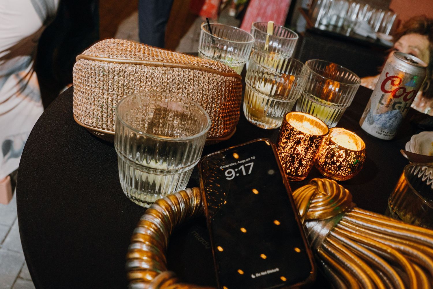 Wedding reception table styled with glass votives, woven clutch purse, candles, and smartphone showing 9:17. New Orleans, Louisiana, Mississ