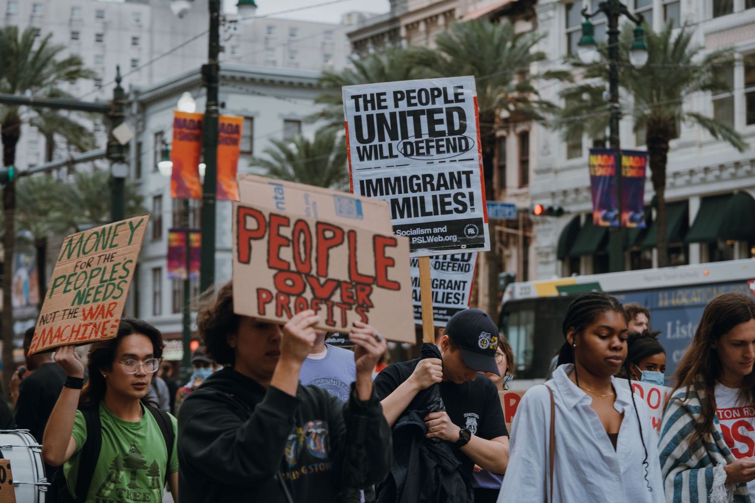 Protesters march through a city street holding signs including one reading People United Will Defend Immigrant Milies.