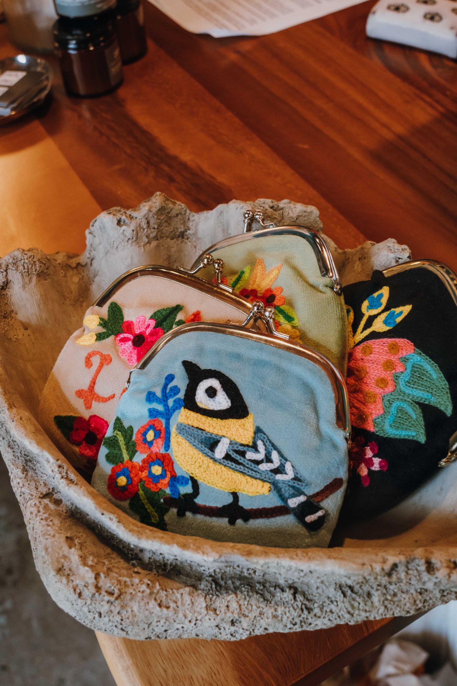 Three embroidered coin purses with floral and bird designs displayed in a stone bowl.