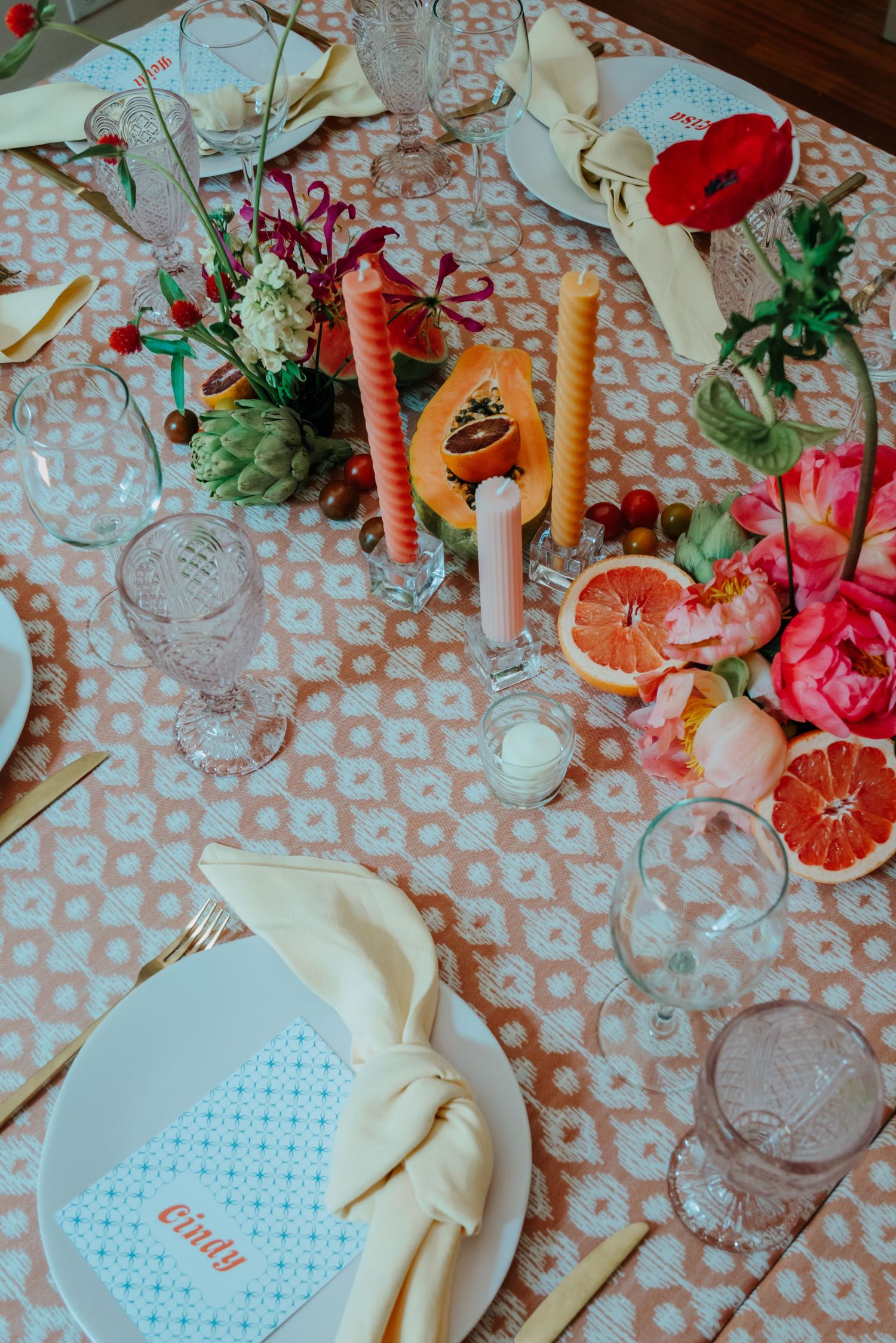 Colorful wedding table setting with floral centerpiece, candles, citrus fruits, and personalized place cards.