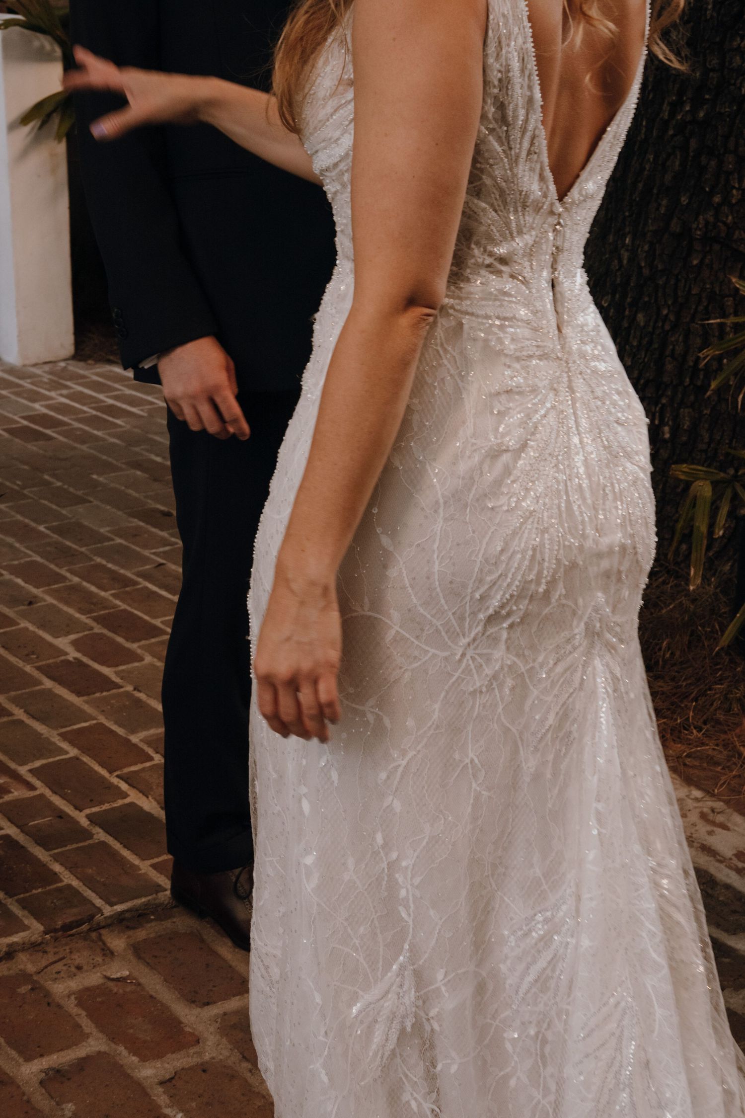 Close-up of bride in a stunning beaded lace backless wedding gown on brick pathway.