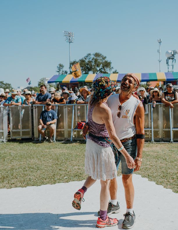 Two festival-goers in colorful bohemian outfits walk together at an outdoor music festival on a sunny day.