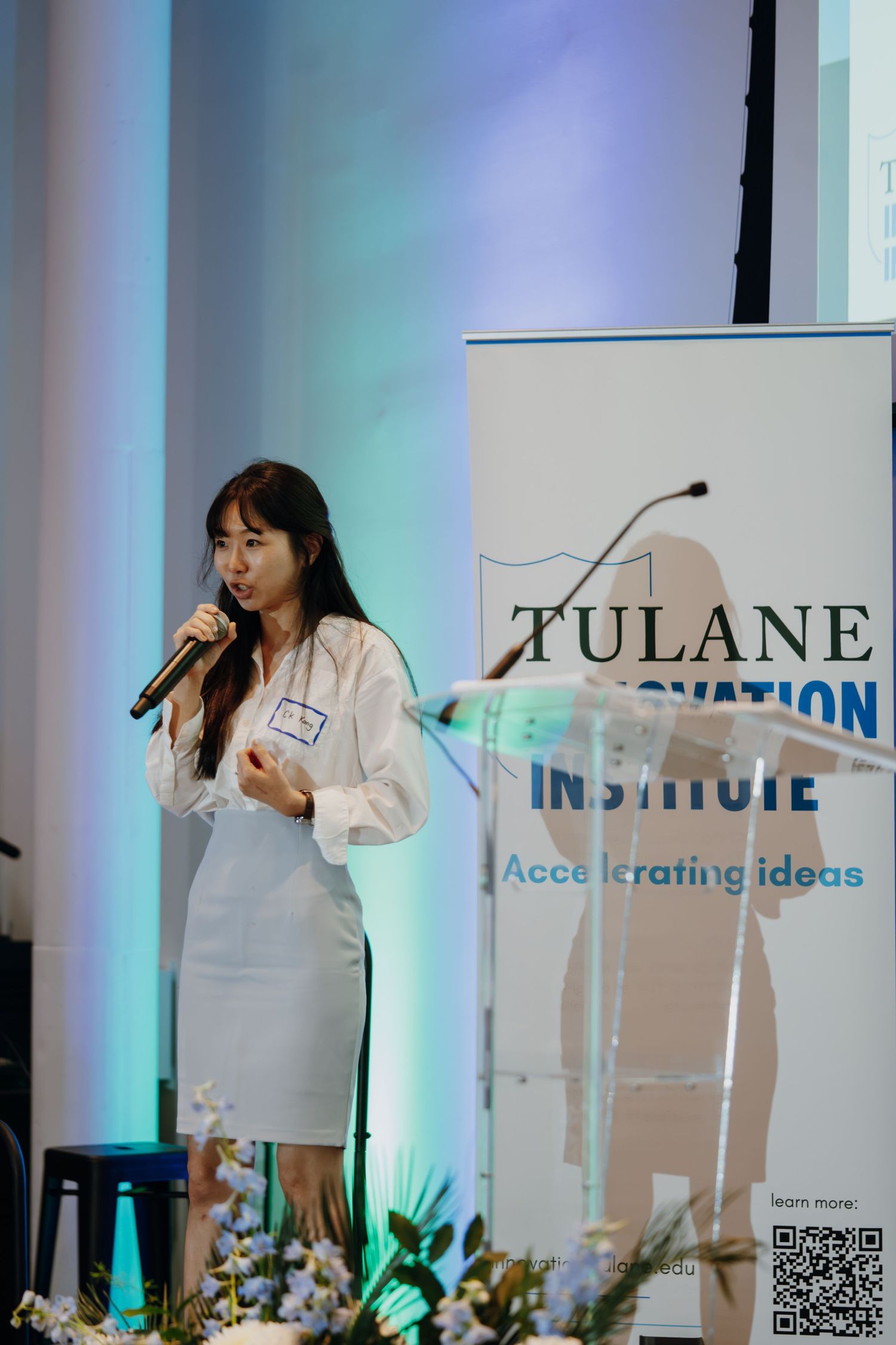 Woman speaking at Tulane Innovation Institute event, holding microphone at podium with banner reading Accelerating Ideas.