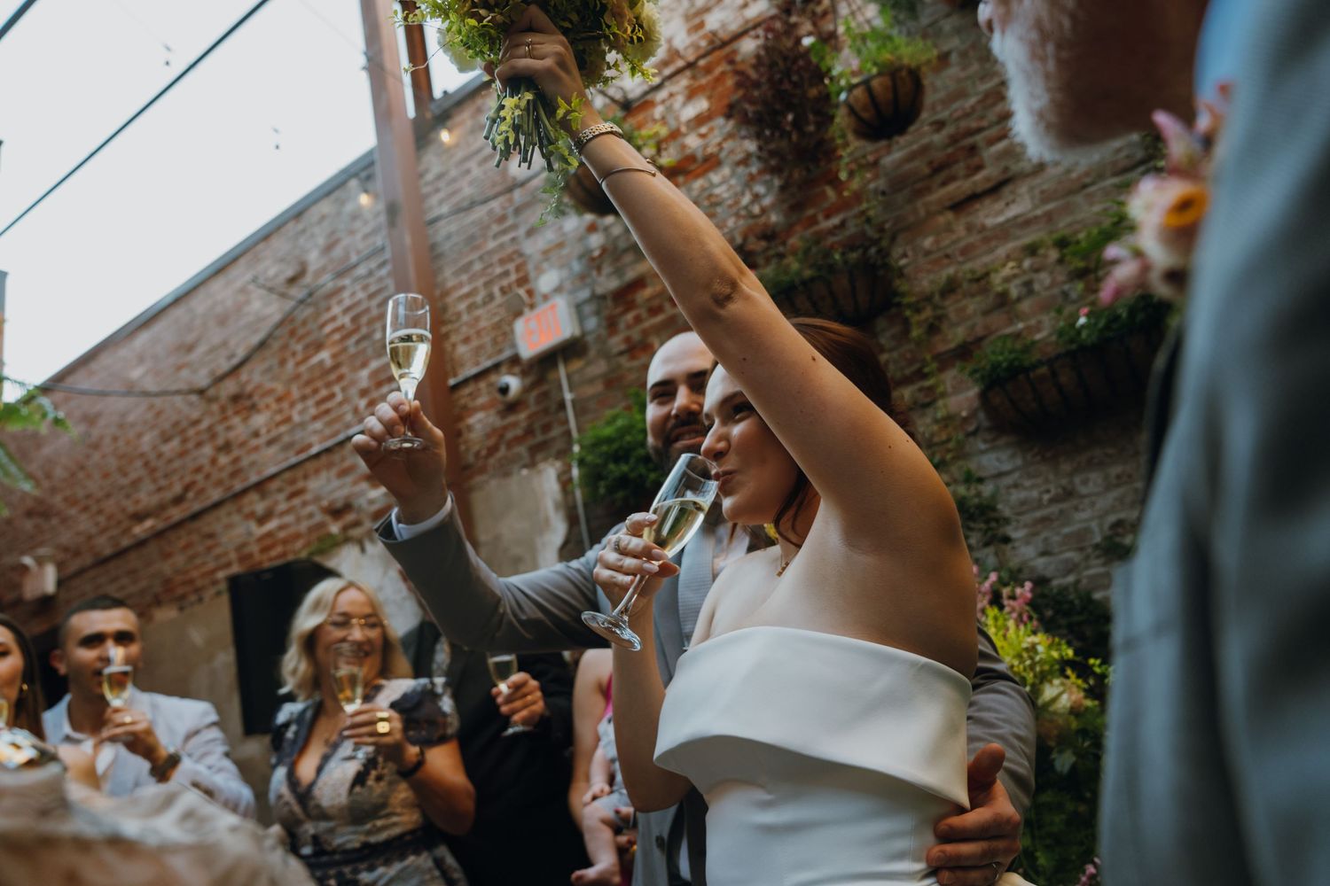 Bride and groom raise champagne glasses in joyful toast with wedding guests in courtyard celebration. New Orleans, Louisiana, Mississippi