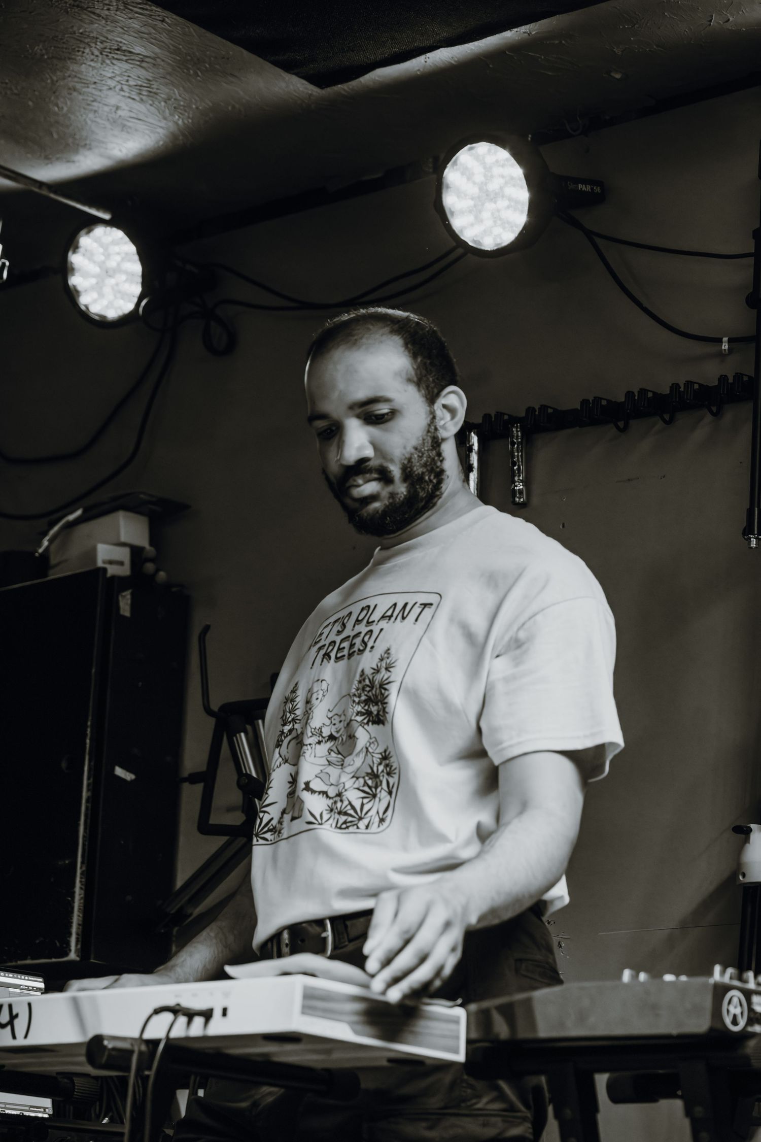 Black and white photo of a bearded man operating a keyboard at a live music venue.