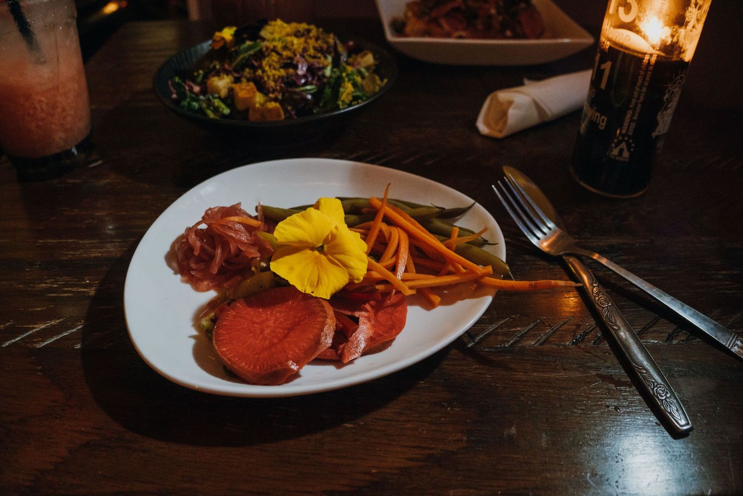 Elegant restaurant plate with sliced cured meat, pickled vegetables, and edible flower garnish on white dish.