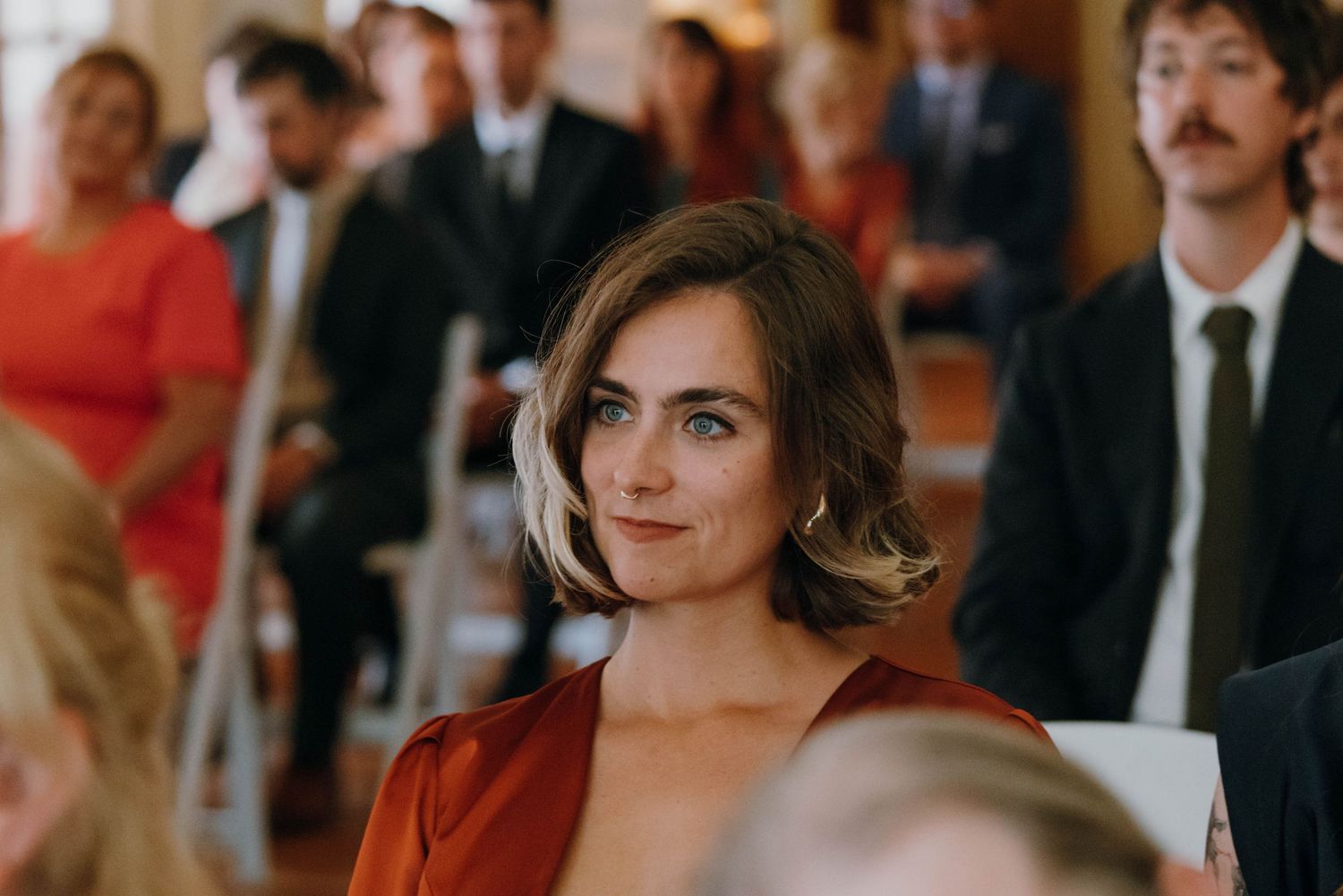 Elegant wedding guest in rust orange dress smiling during wedding ceremony.