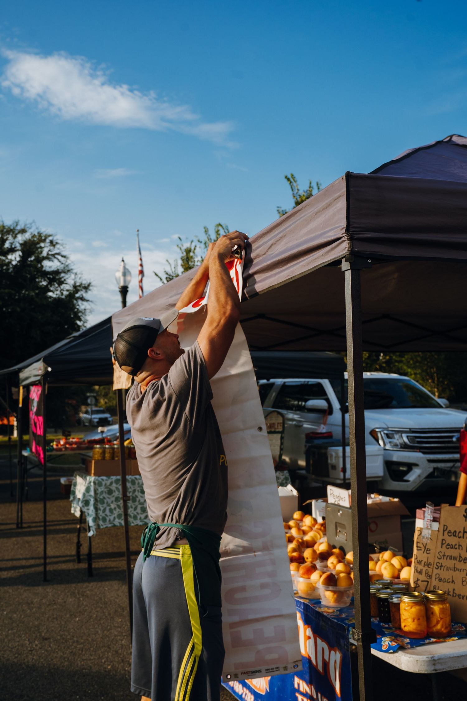 Vendor sets up canopy tent at outdoor farmers market on sunny day.